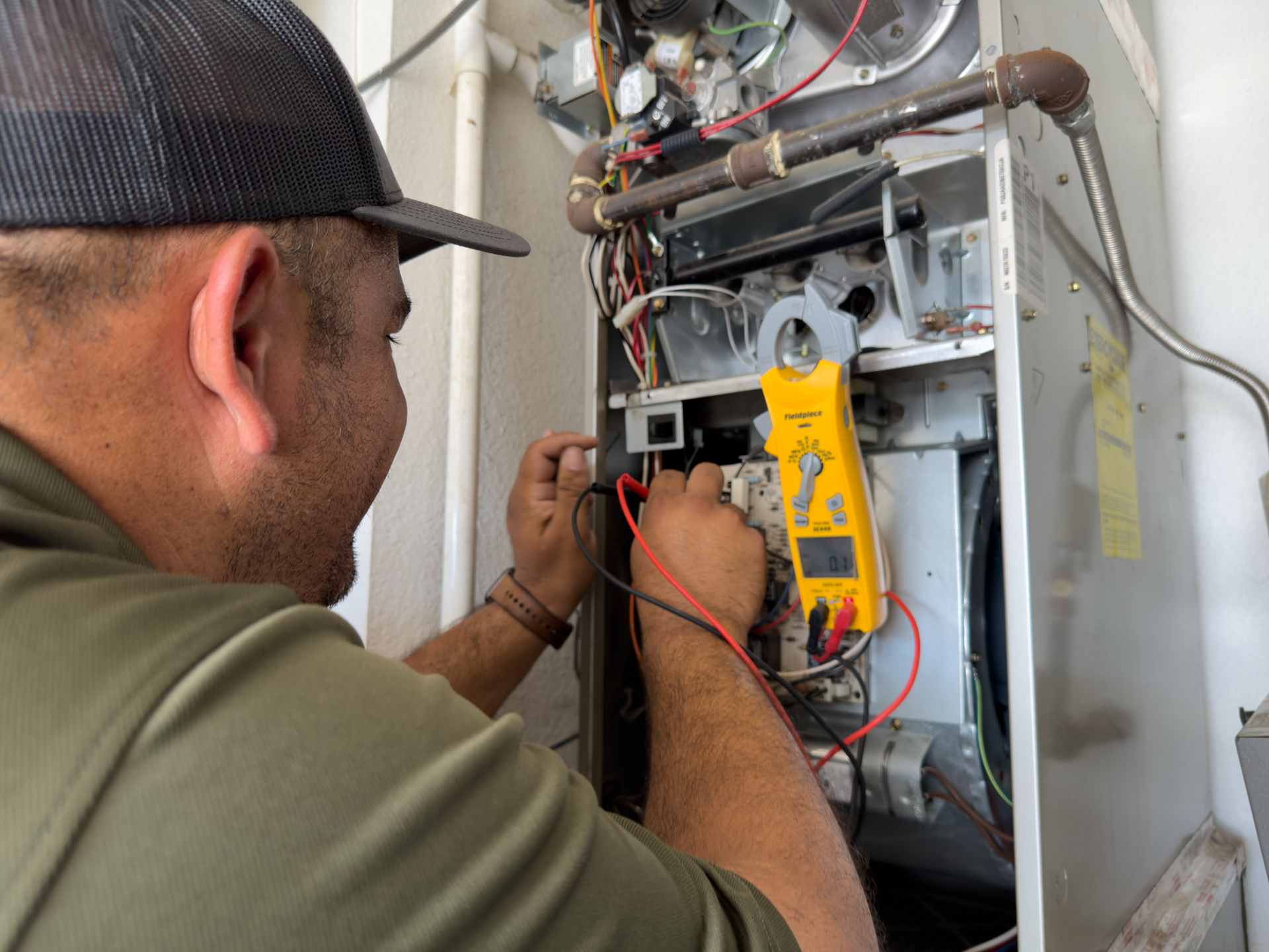 Technician inspecting furnace wiring with a yellow multimeter in an open utility cabinet