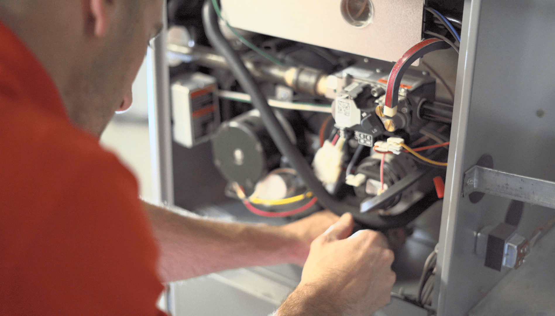 Technician in orange shirt repairing electrical wiring inside a machine cabinet