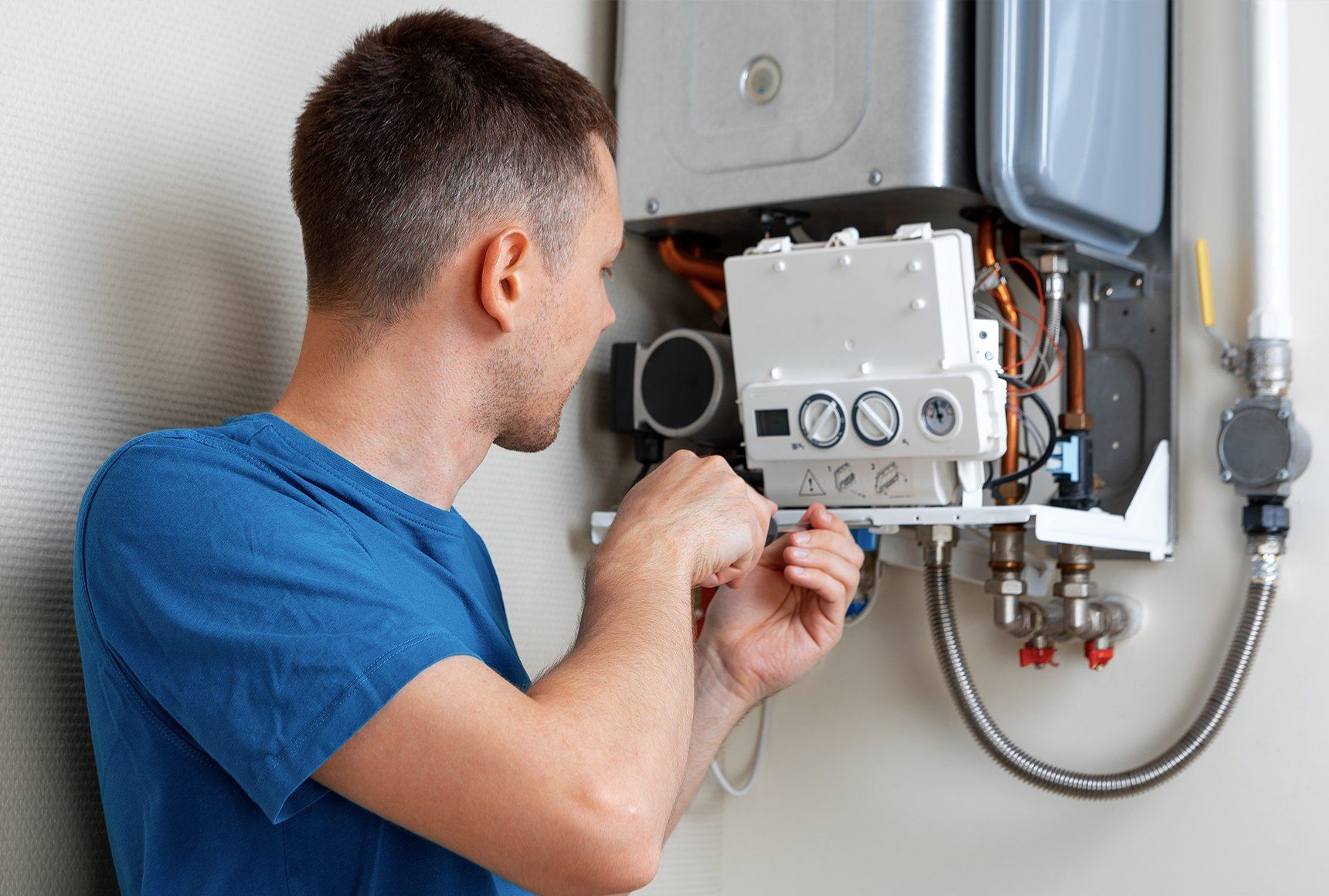Technician adjusting a wall-mounted gas water heater with a wrench