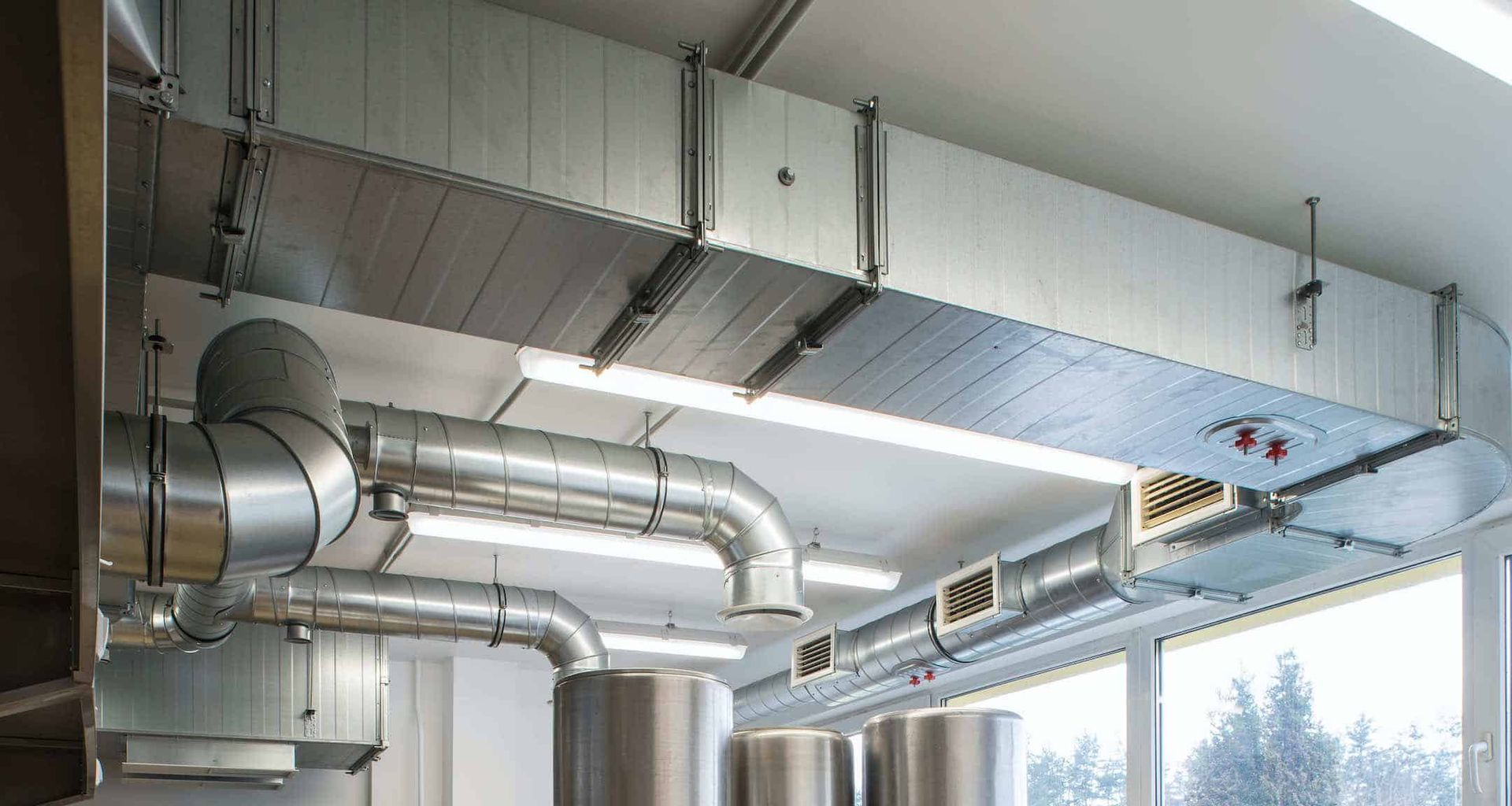 Industrial ceiling ductwork and HVAC vents in a bright room with large windows