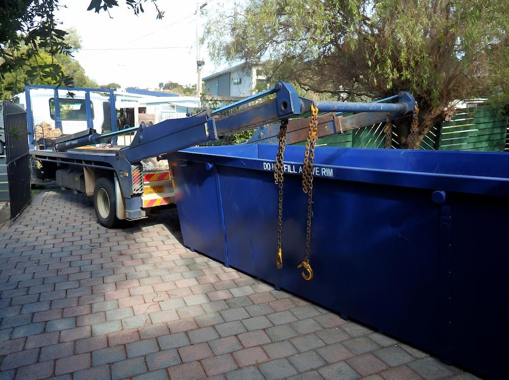 A Blue Dumpster is Sitting on a Brick Driveway Next to a Truck — Alexander Crane Tippers in Yass, NSW