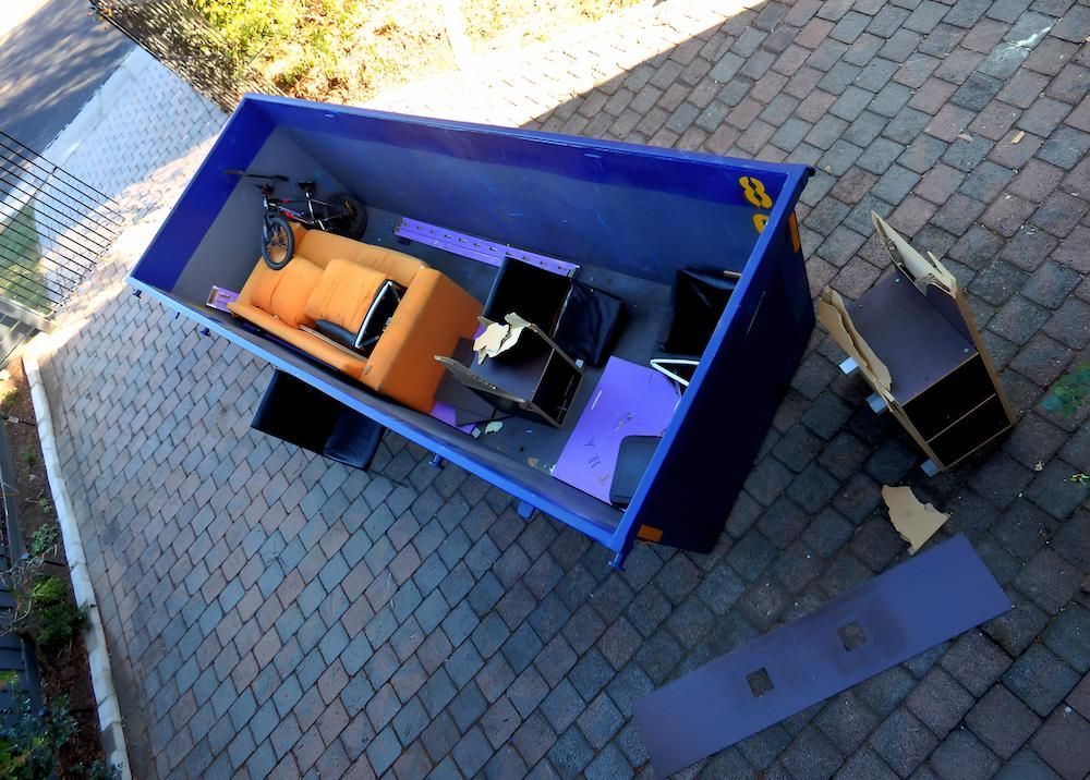 A Blue Dumpster Filled With Furniture and a Bicycle — Alexander Crane Tippers in Bungendore, NSW