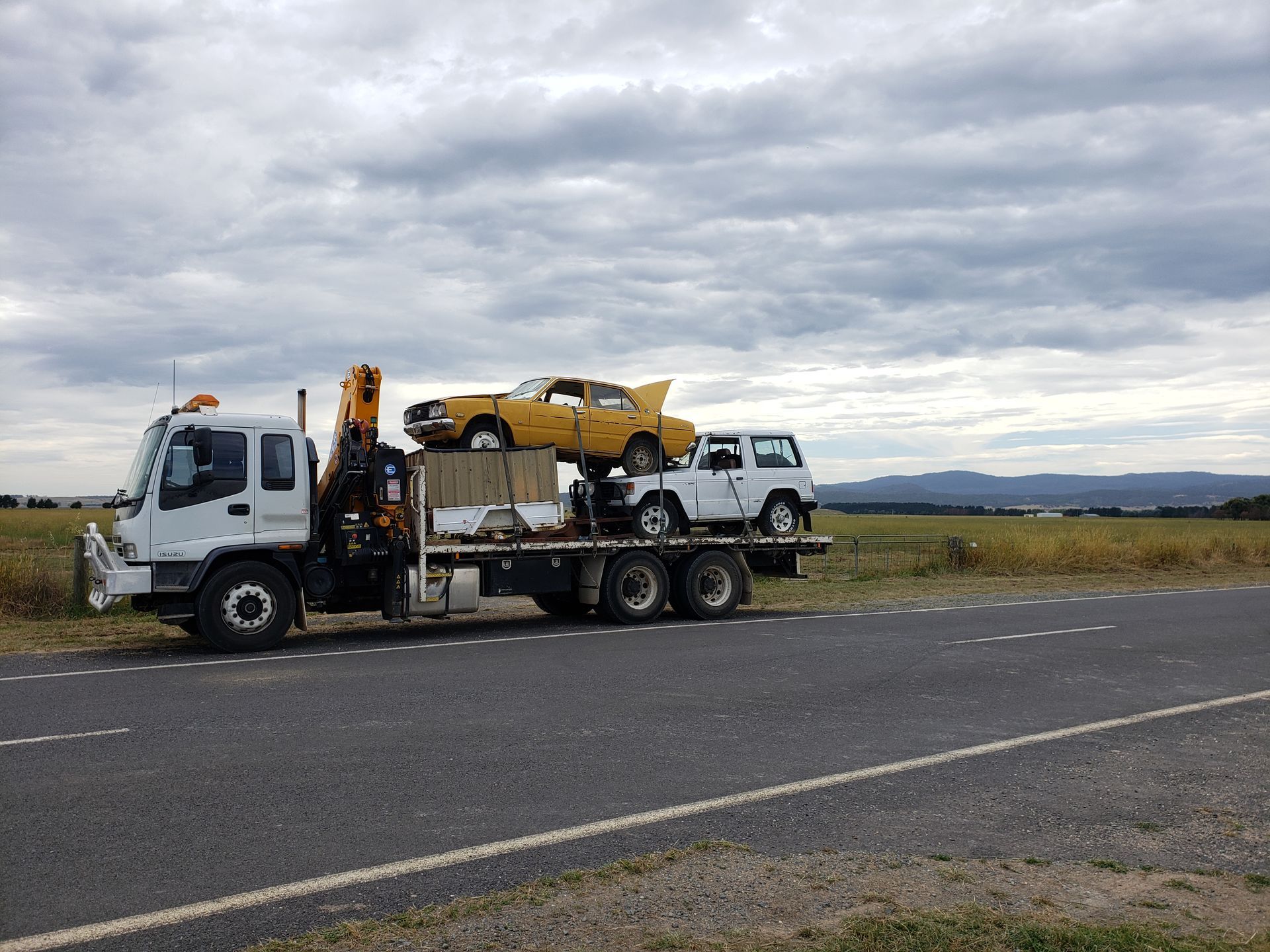 A Tow Truck is Carrying a Yellow Car on the Back of It — Alexander Crane Tippers in Latham, ACT