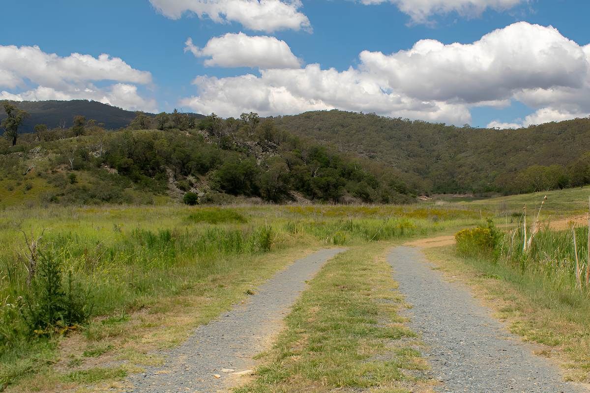 A Dirt Road Going Through a Grassy Field With Mountains in the Background — Alexander Crane Tippers in Googong, NSW