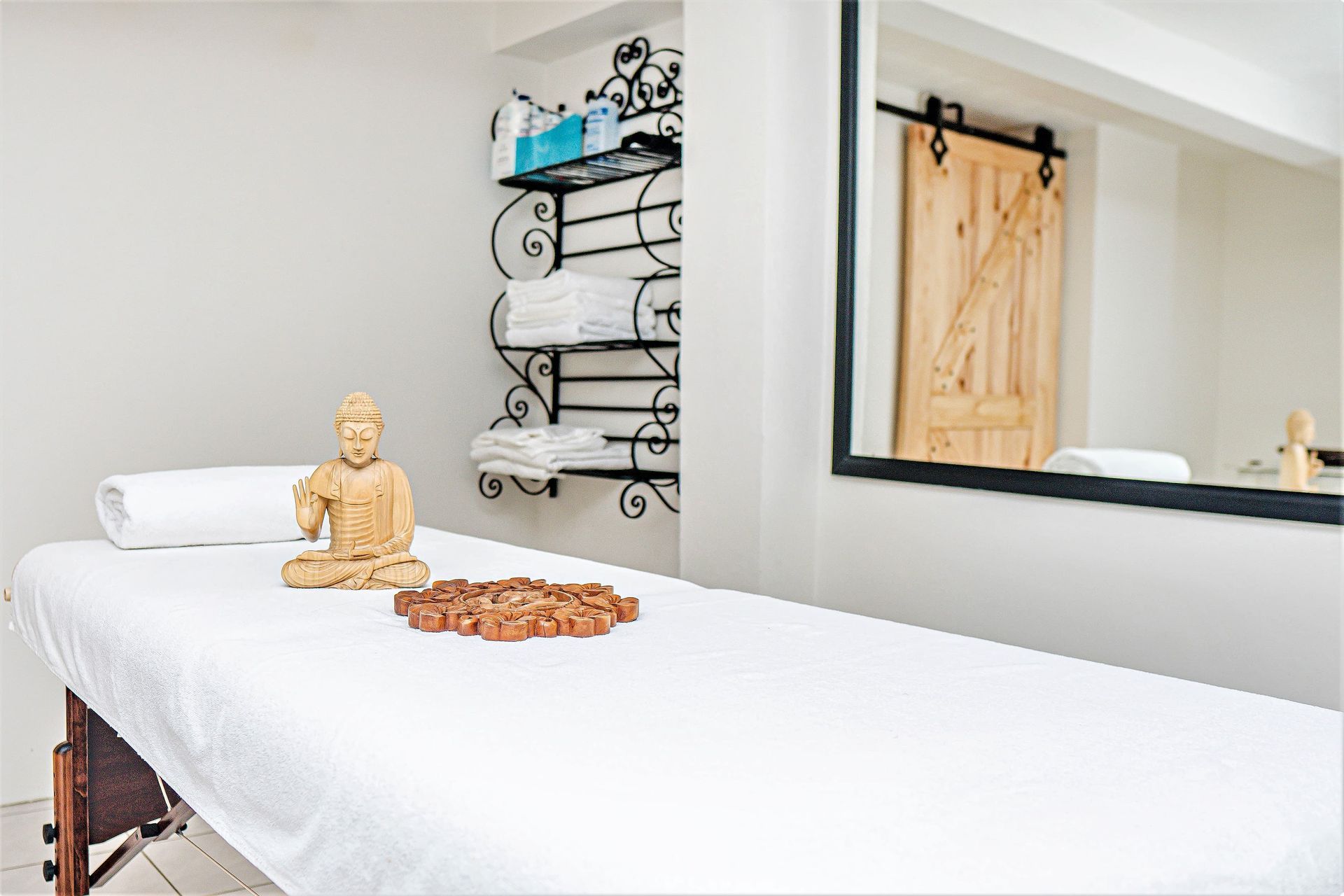Massage room with white sheets, wooden Buddha, and towels.