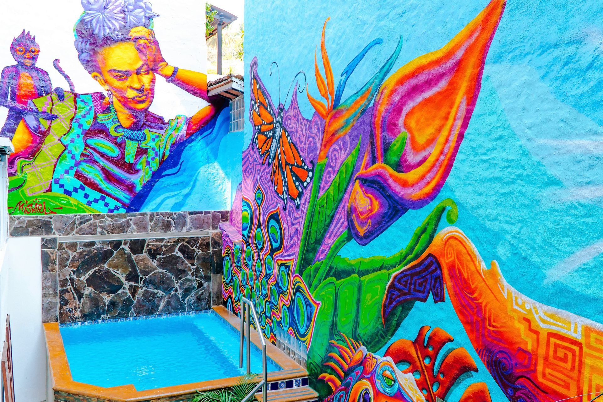 A mural of frida kahlo is painted on the side of a building next to a pool.