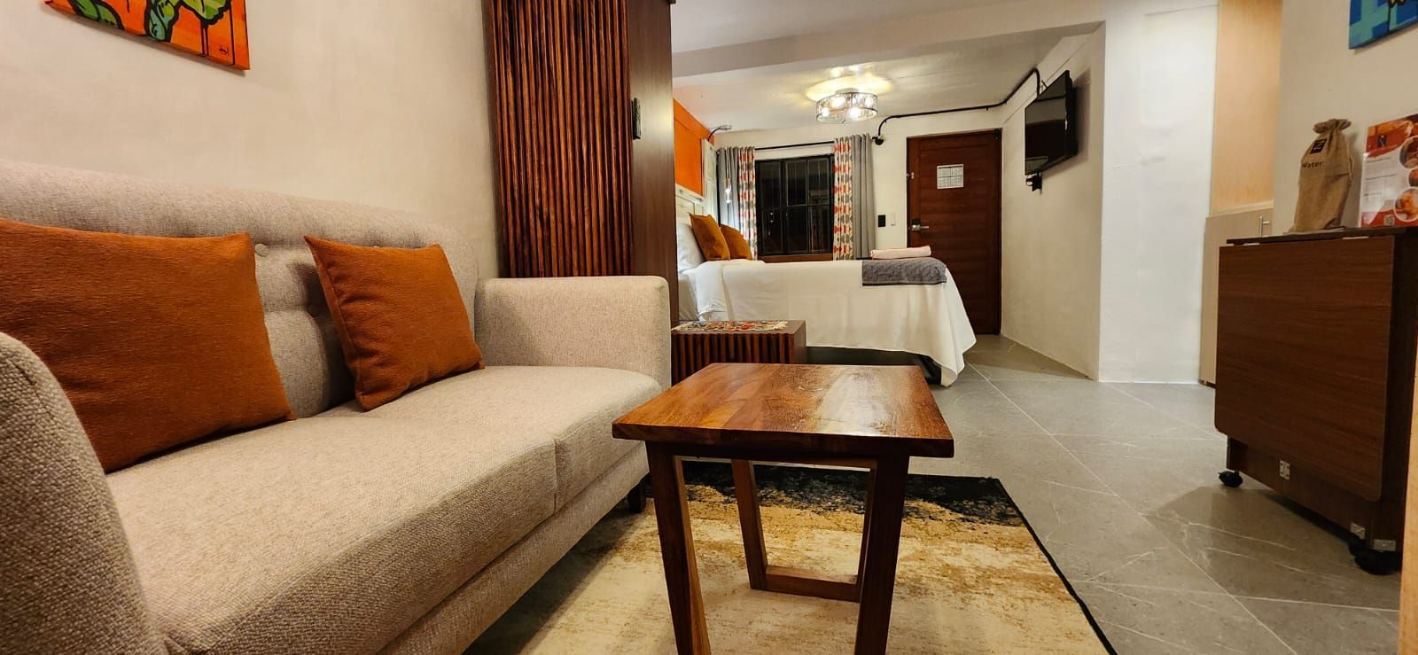 Cozy hotel room with a sofa, bed, wooden table, and brown curtains.