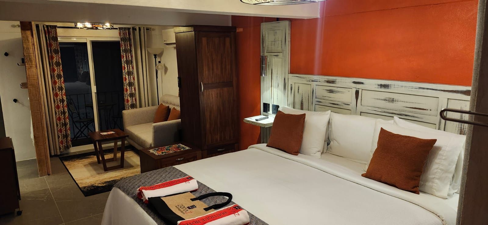 Hotel room with a bed, seating area, and orange accent wall. Dark wooden furniture.