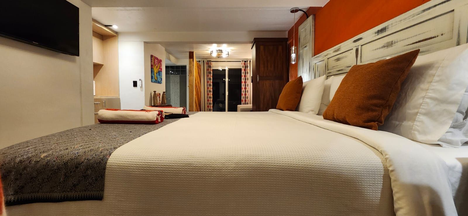 Bedroom with large bed, orange accent wall, TV, and doorway to outside.