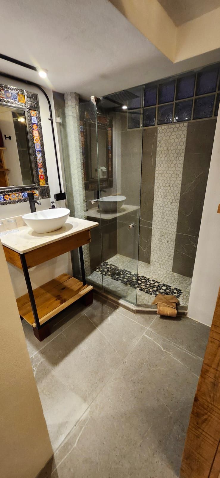 A modern bathroom with a glass shower, stone tiles, and a wooden vanity.