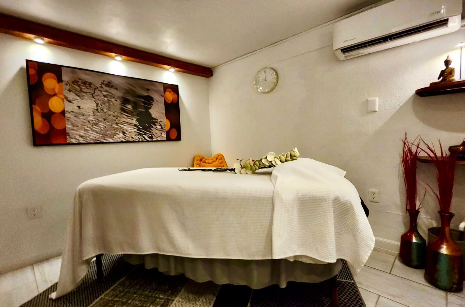 Massage room with white linens, artwork, vases, and a clock.