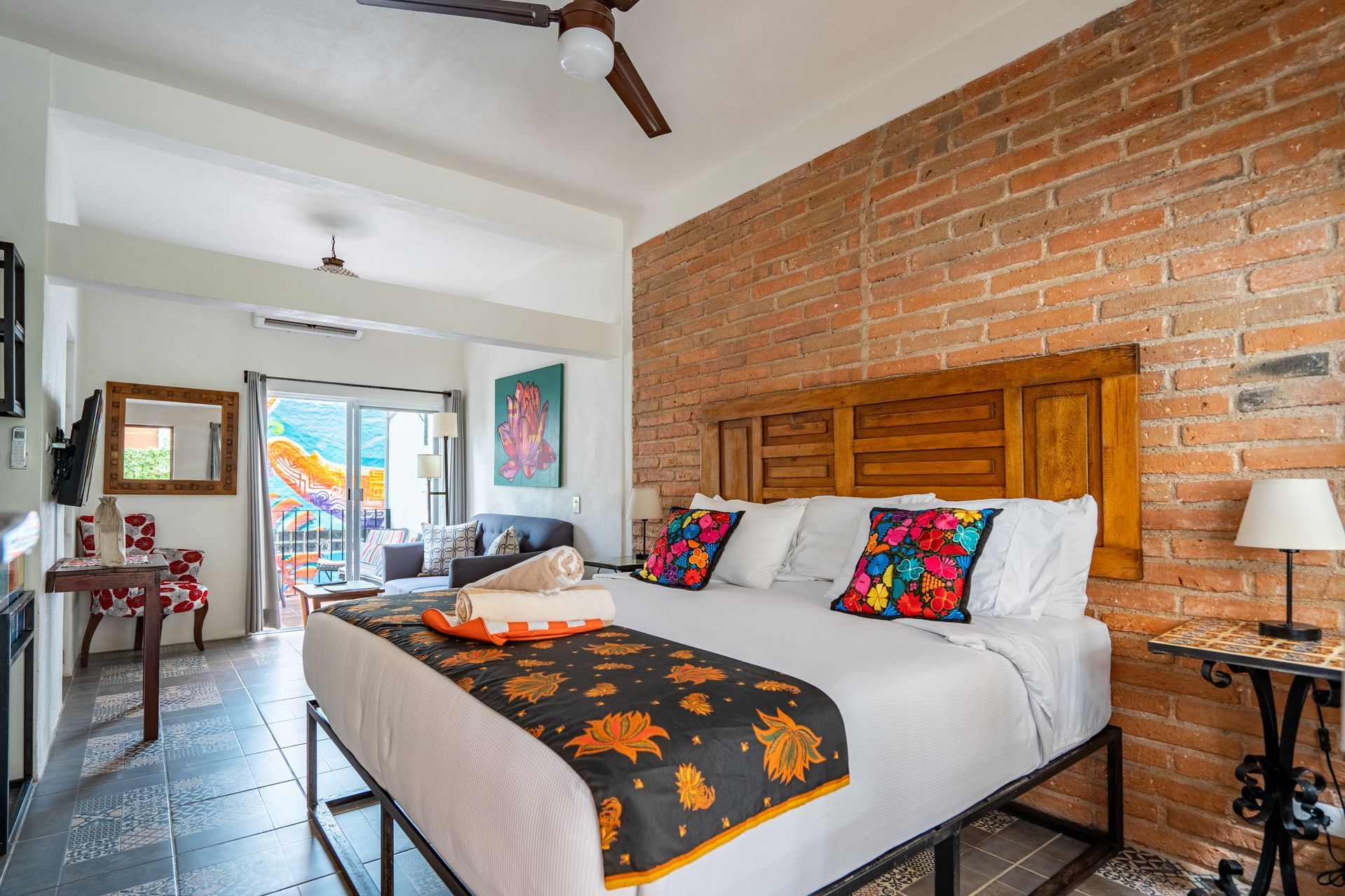 Bedroom with exposed brick wall, king bed with colorful pillows, and a balcony.