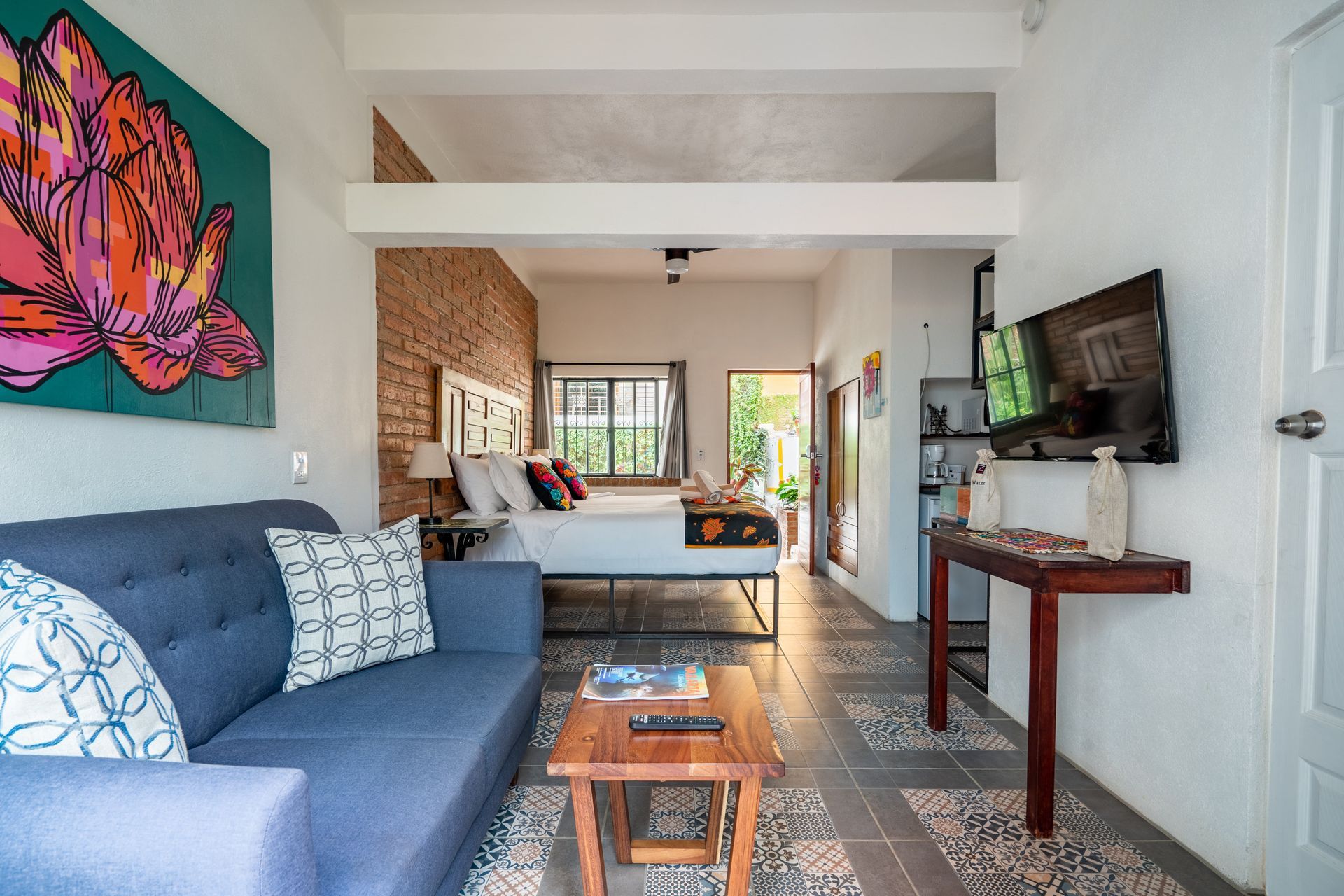 Blue sofa in colorful studio apartment with bed, TV, and artwork.