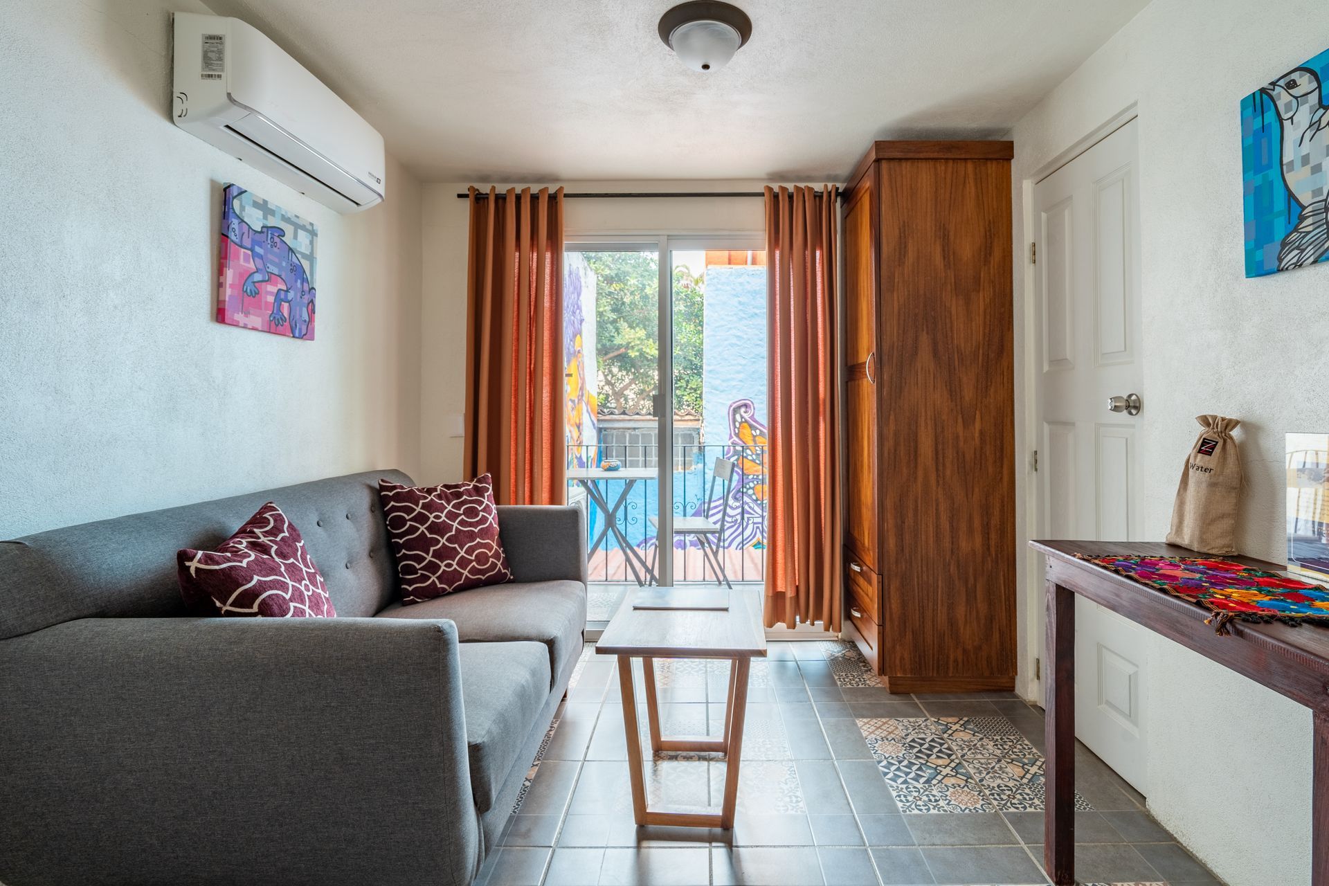 Gray sofa, wooden cabinet, and sliding door open to balcony in a brightly lit room.