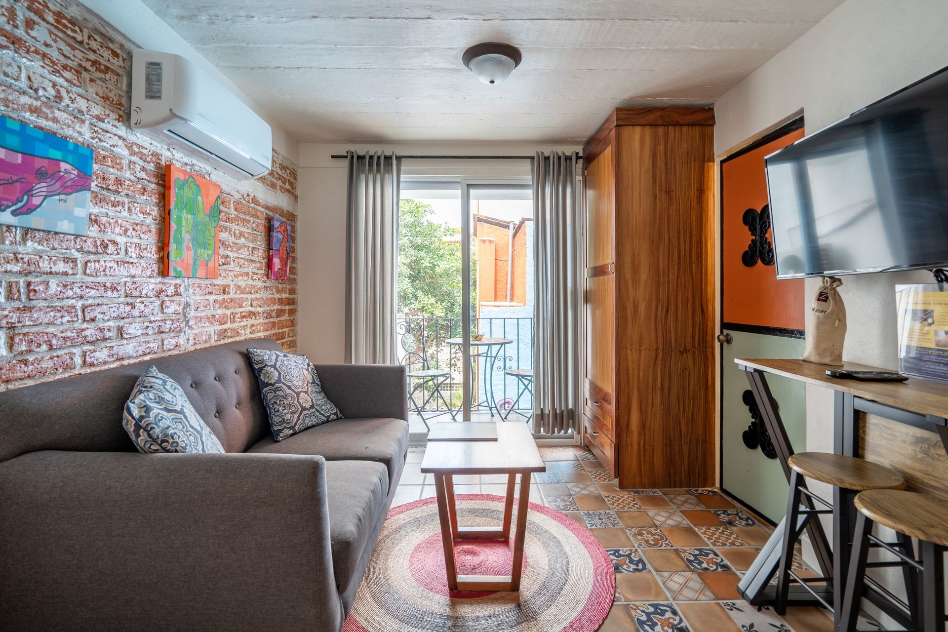 Living room with brick wall, gray sofa, TV, and balcony access.