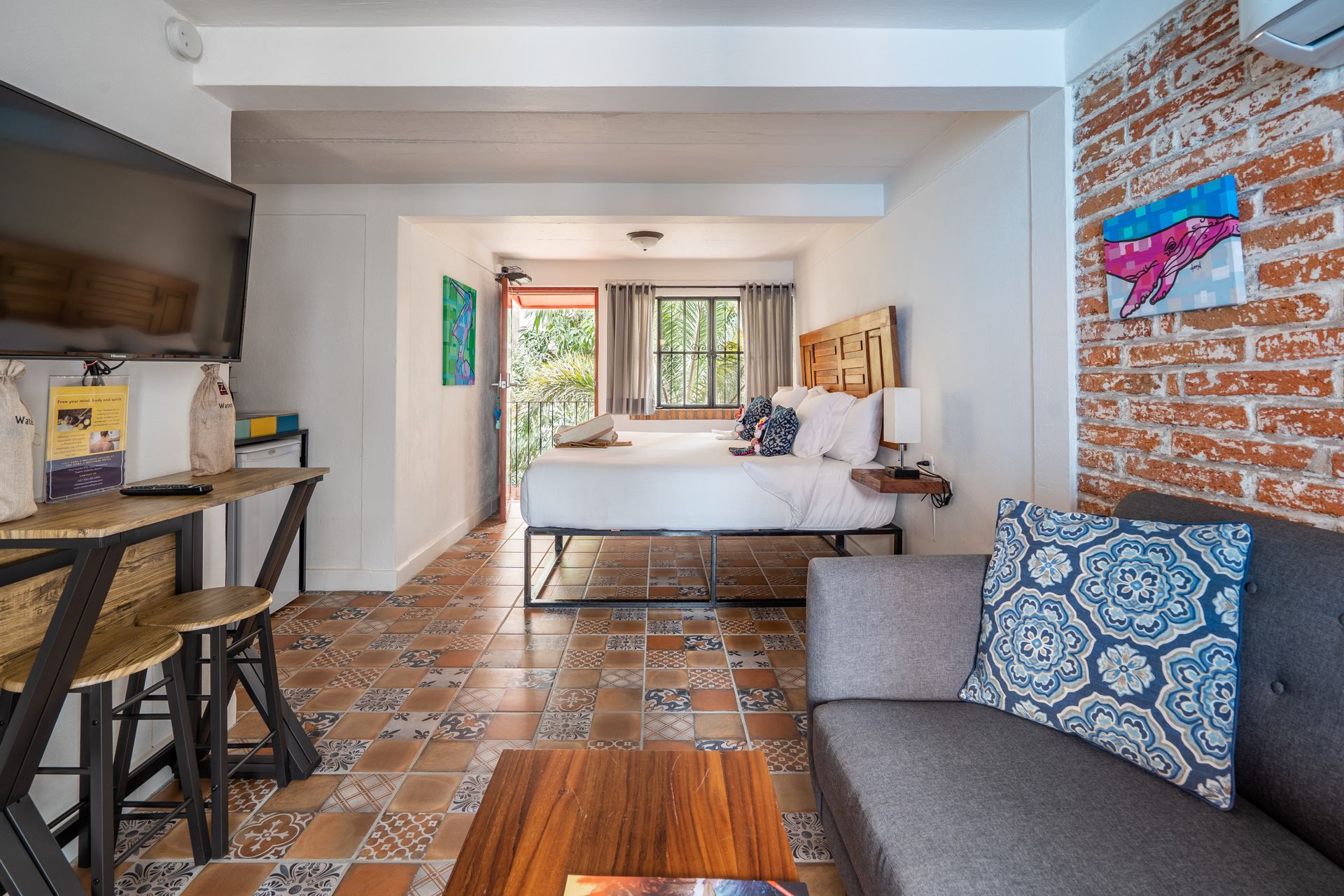 Cozy studio apartment with bed, sofa, brick wall, TV, and breakfast bar.