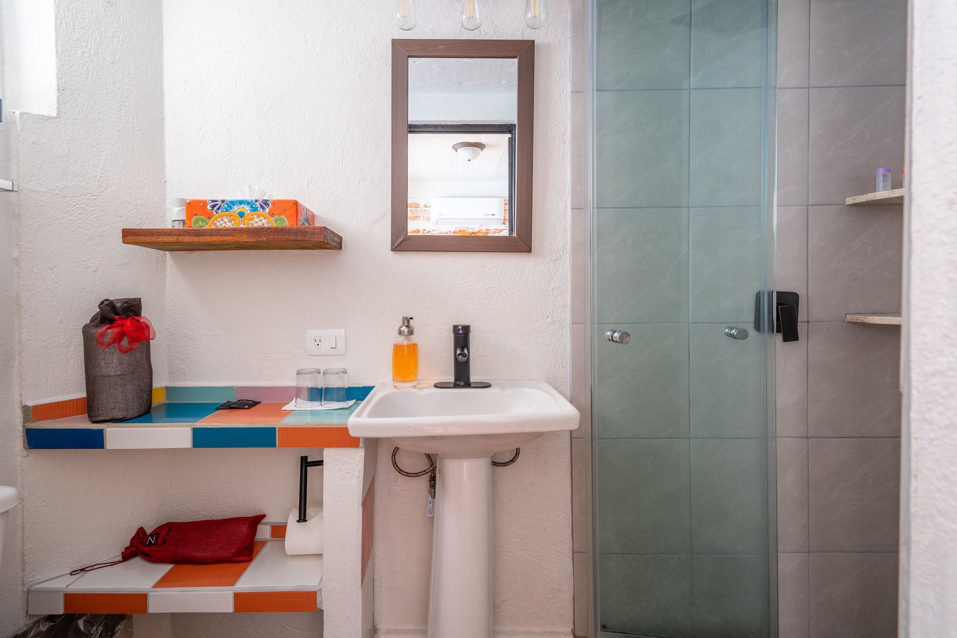 Bathroom with a pedestal sink, a shower with glass doors, and colorful shelf detailing.