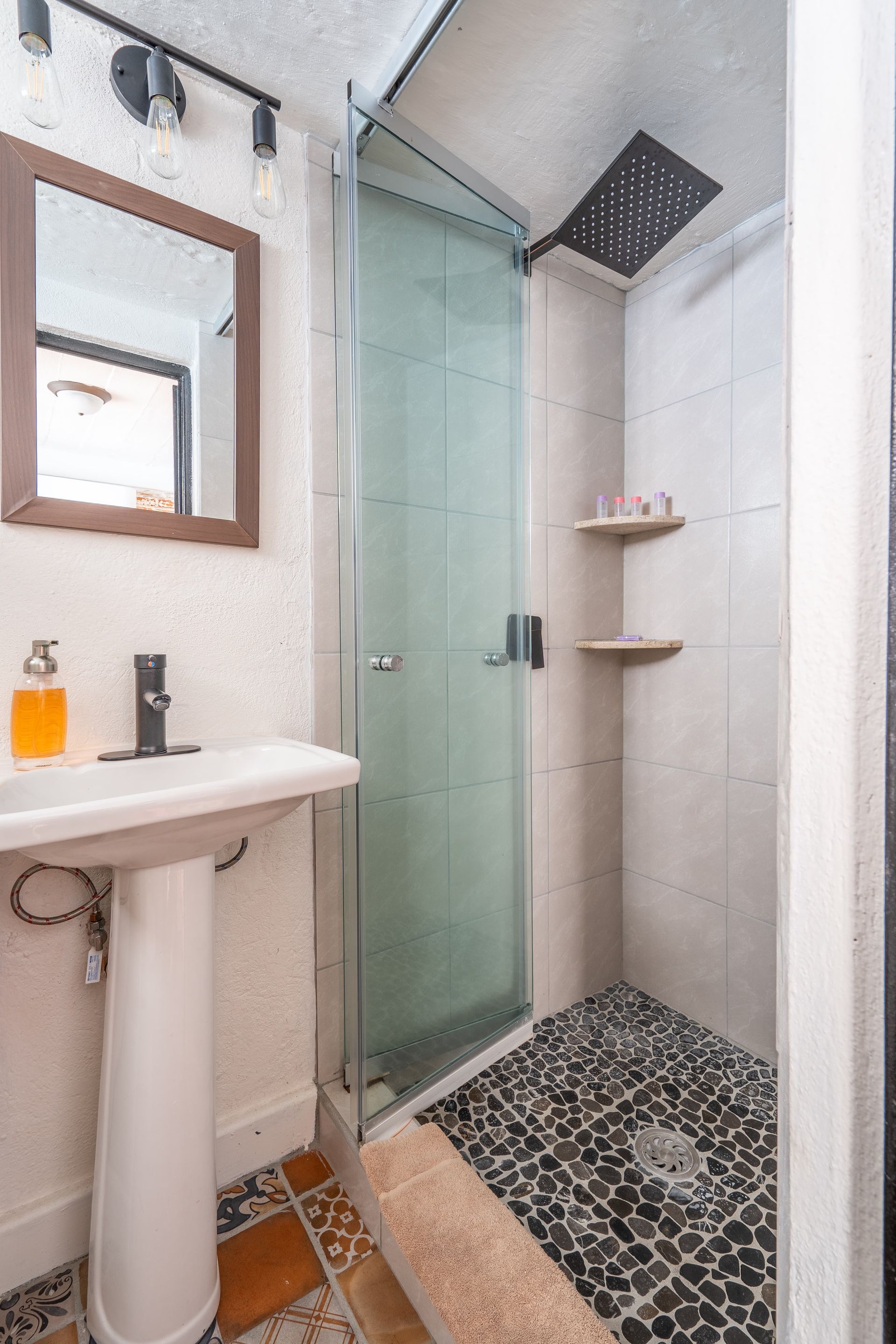 Bathroom with pedestal sink, shower stall, and pebble floor.