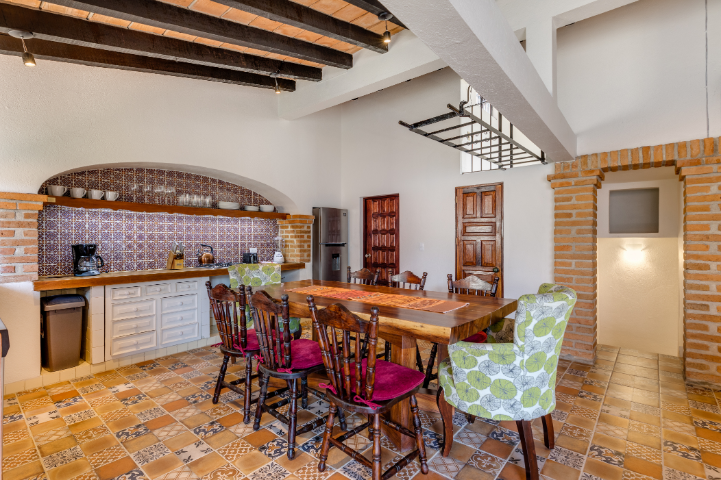 A dining room with a table and chairs and a kitchen.