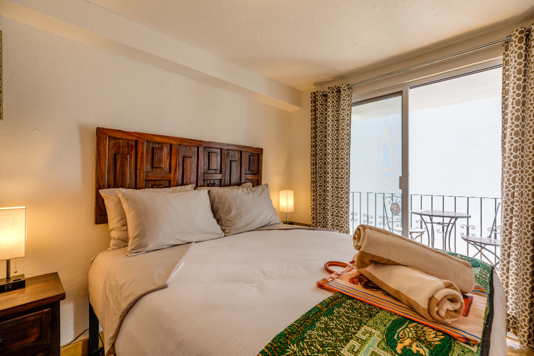 A bedroom with a large bed and a sliding glass door leading to a balcony.
