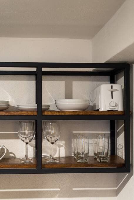 A shelf with plates , glasses , a toaster and a bowl on it.