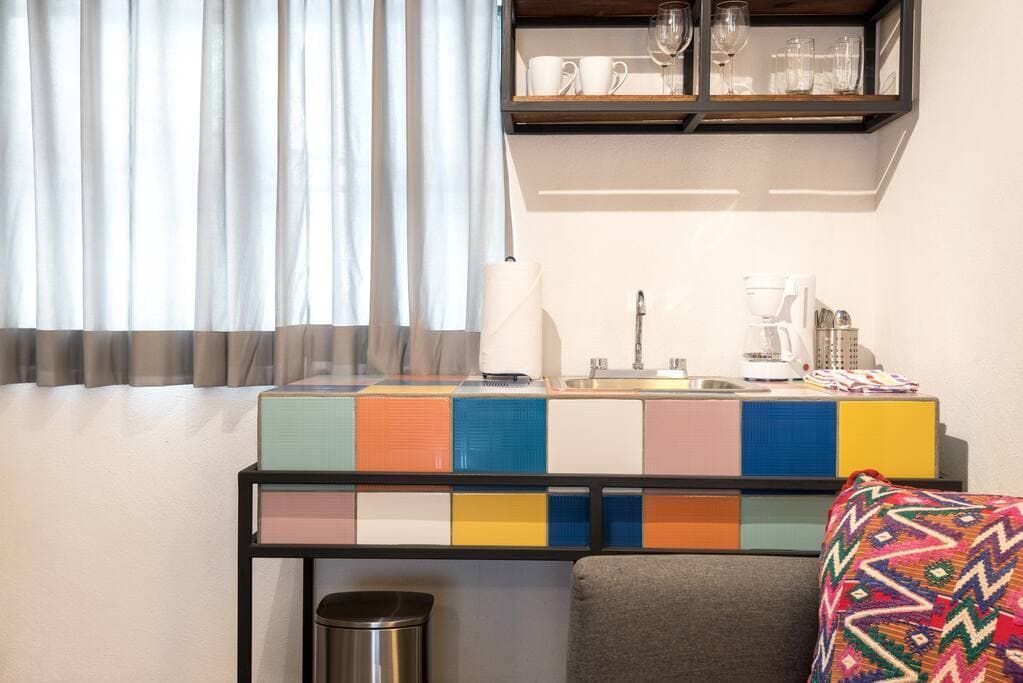 A living room with a couch , desk , sink and window.