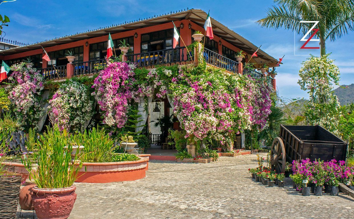 A house with a lot of flowers and a wagon in front of it.