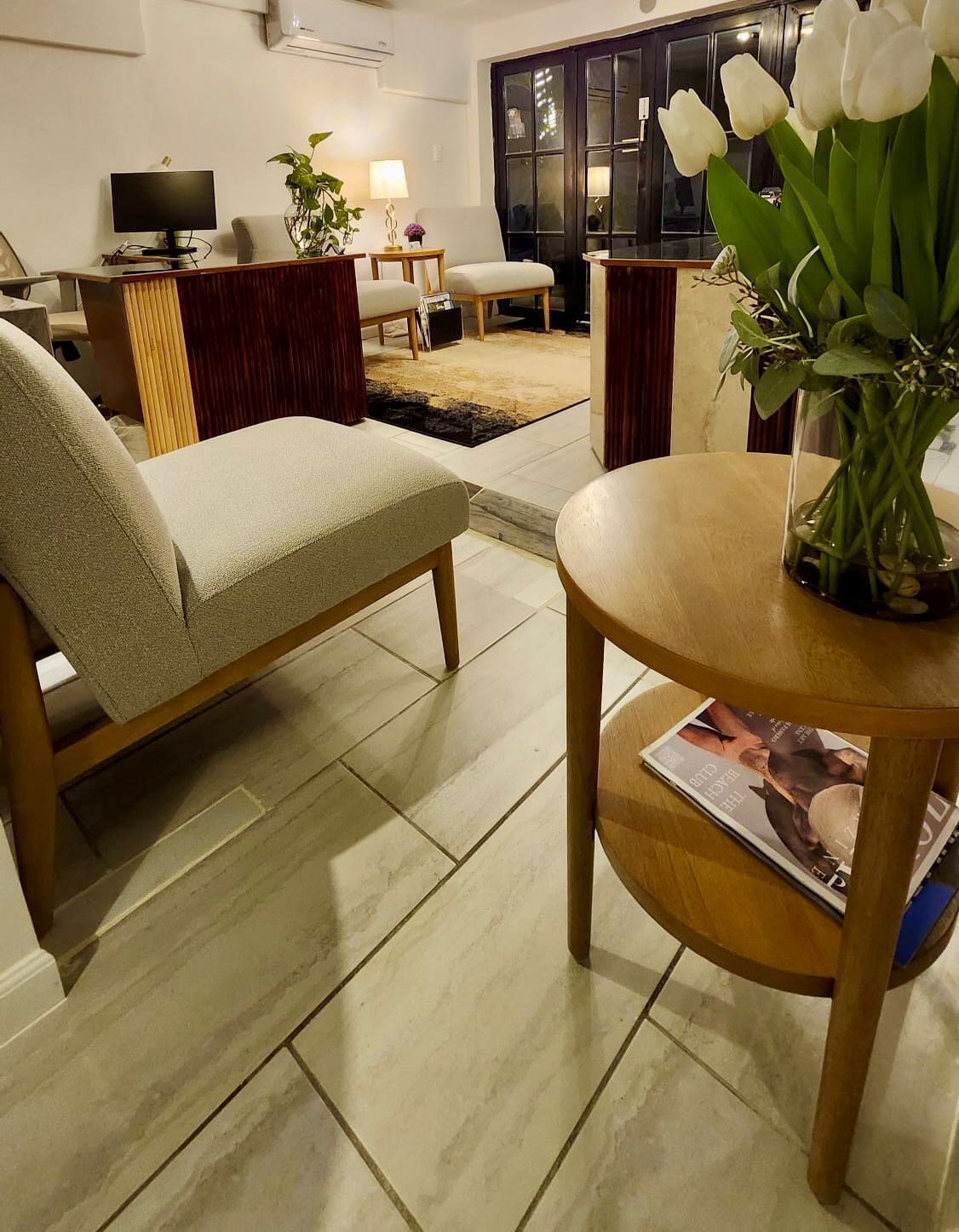 Cozy living room with a light-colored chair, wooden table with tulips, and a view of the outdoors.