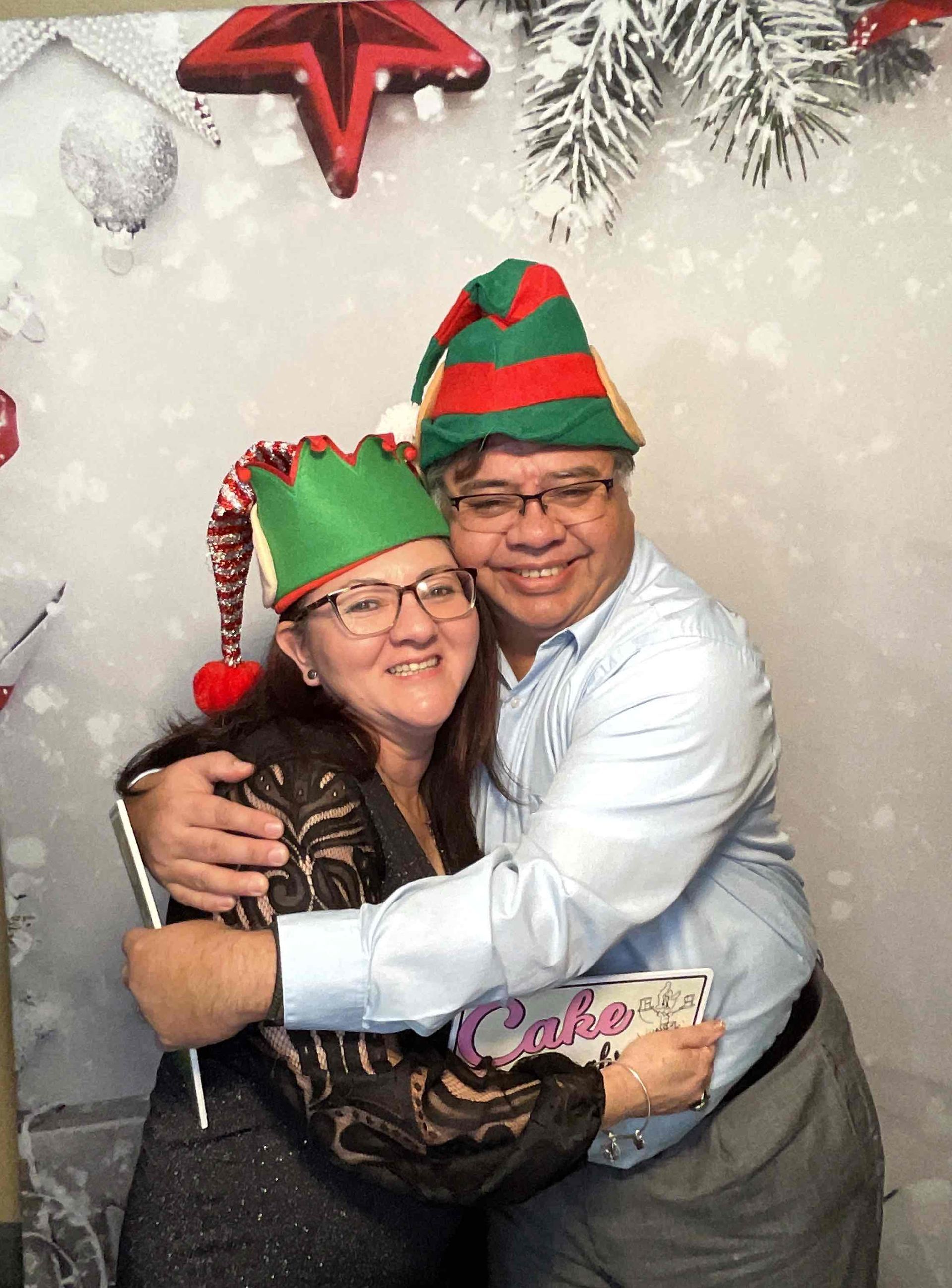 A man and a woman wearing elf hats are hugging each other.
