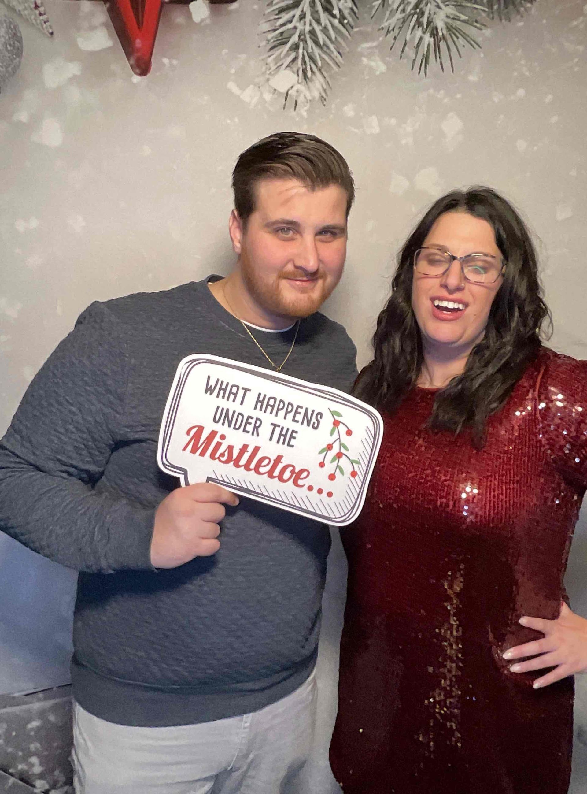 A man and a woman are standing next to each other holding a sign that says what happens under the mistletoe.