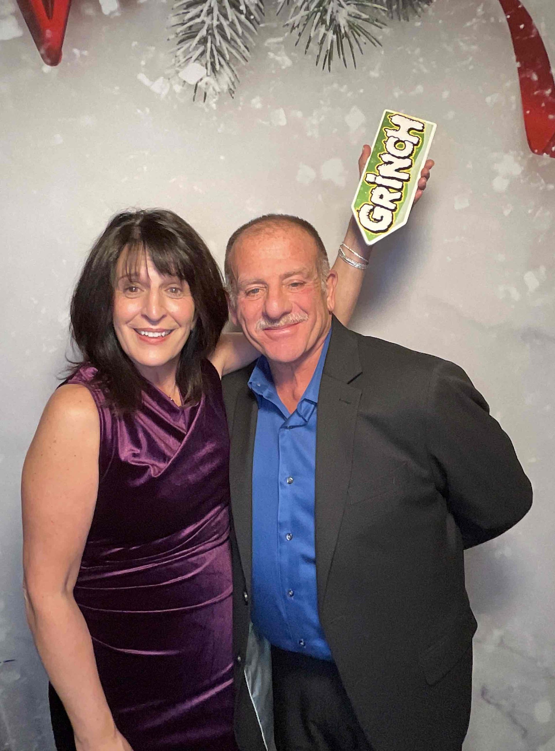 A man and a woman are posing for a picture in front of a grinch sign.