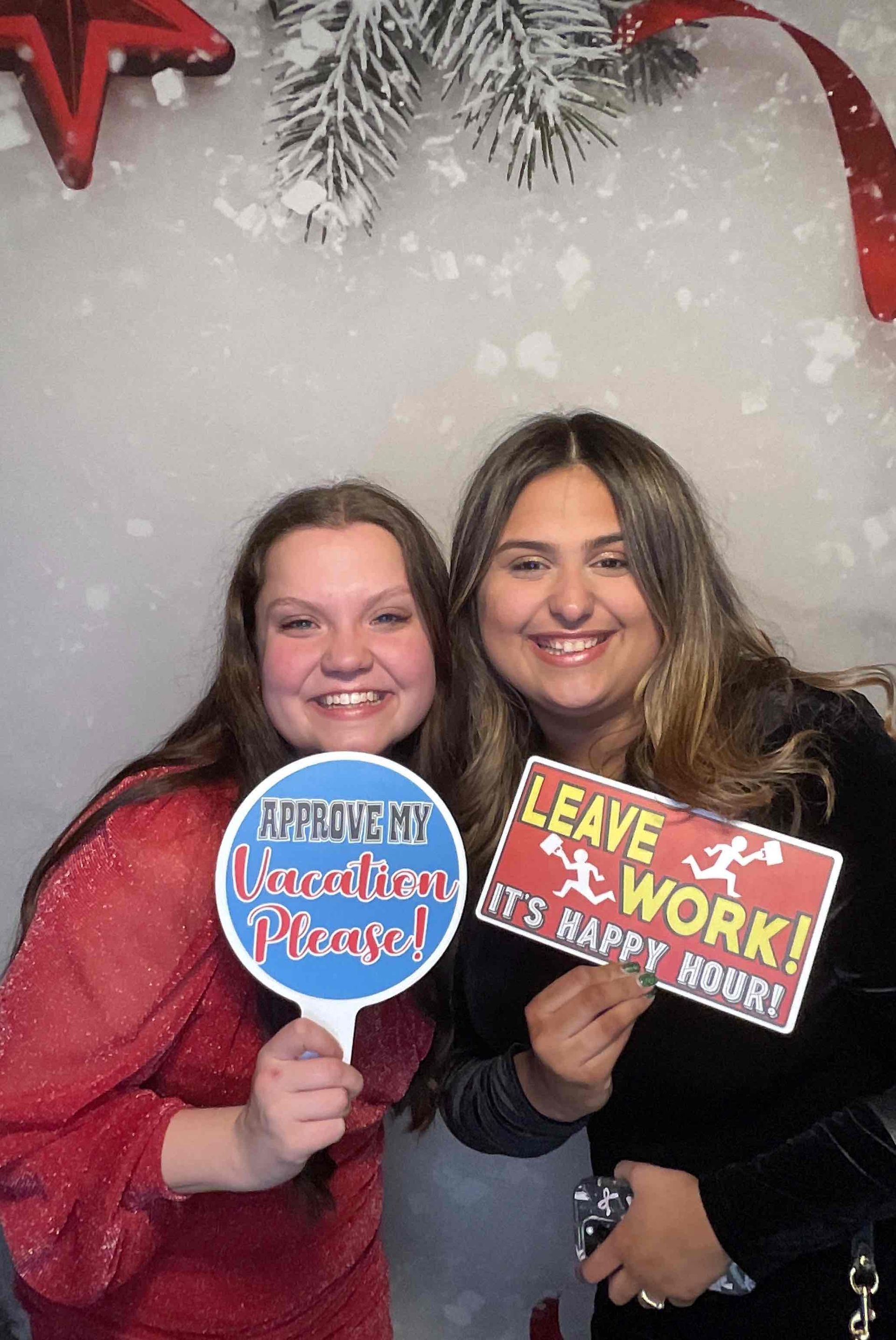 Two women are posing for a picture in a photo booth holding signs.