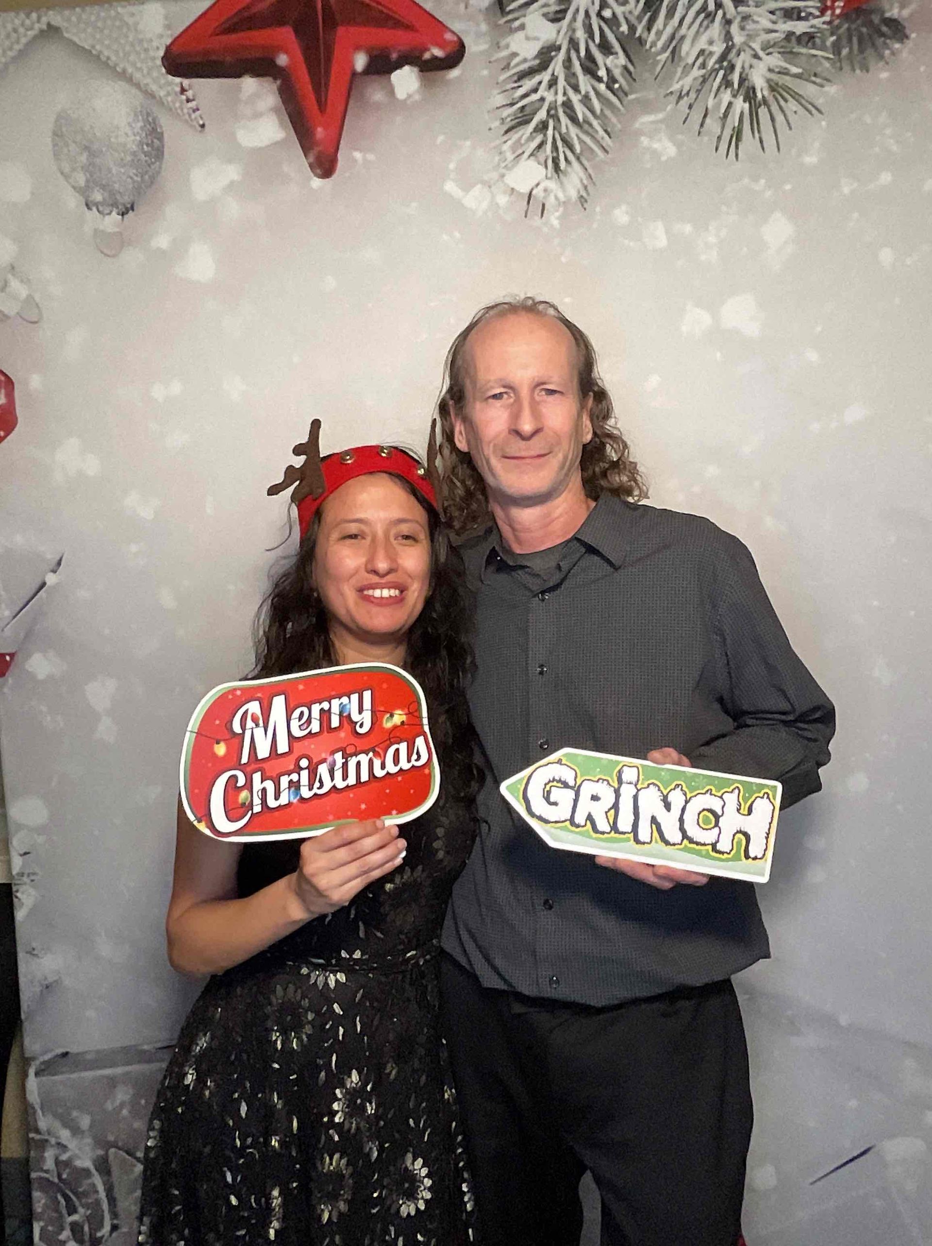 A man and a woman are holding signs that say merry christmas and grinch.