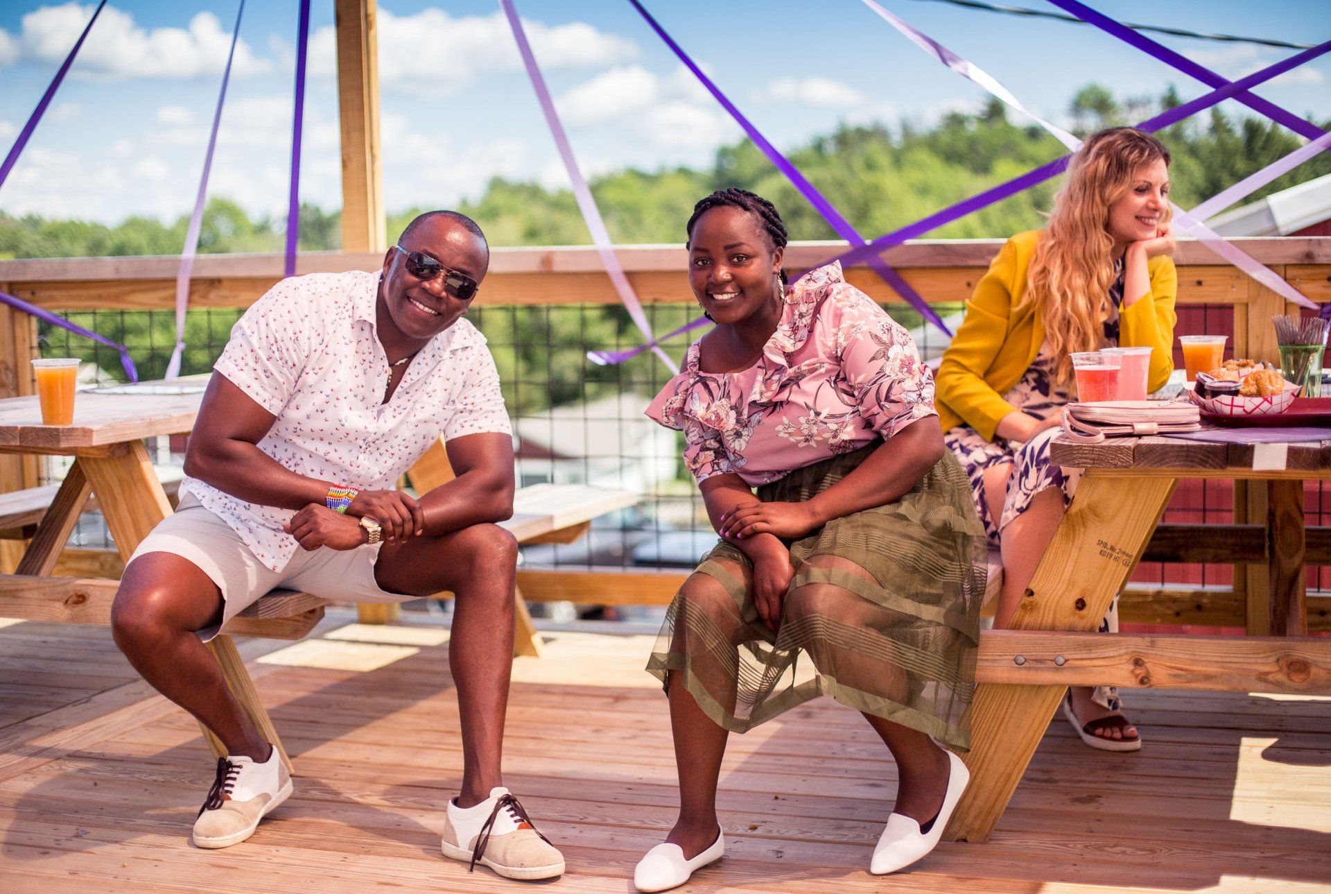 A man and two women are sitting on a wooden picnic table.