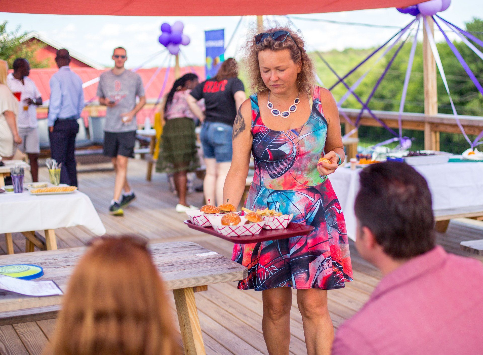 A woman is carrying a tray of food to a group of people at a party.