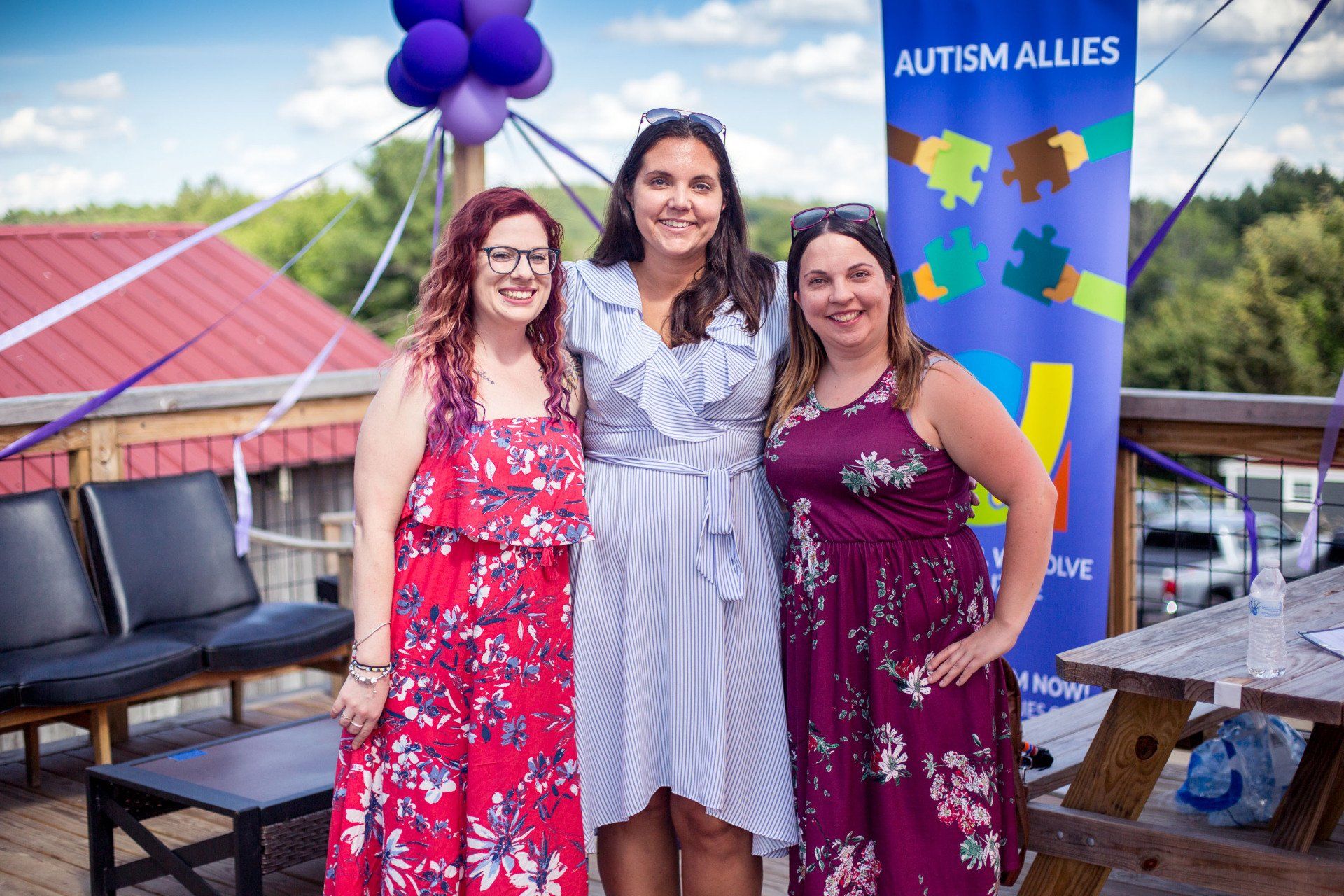 Three women are posing for a picture in front of a sign that says autism allies.