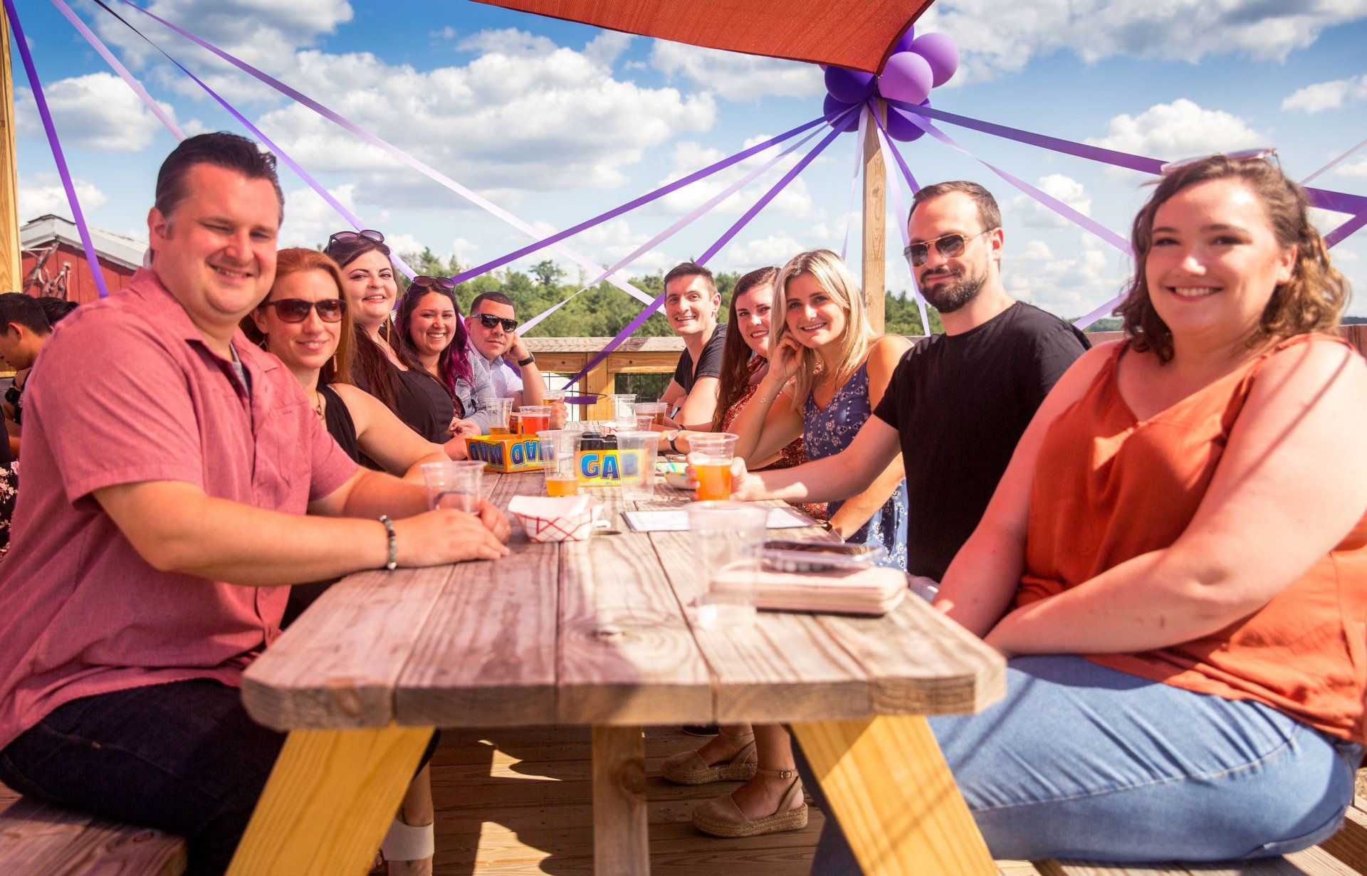 A group of people are sitting at a picnic table under an umbrella.