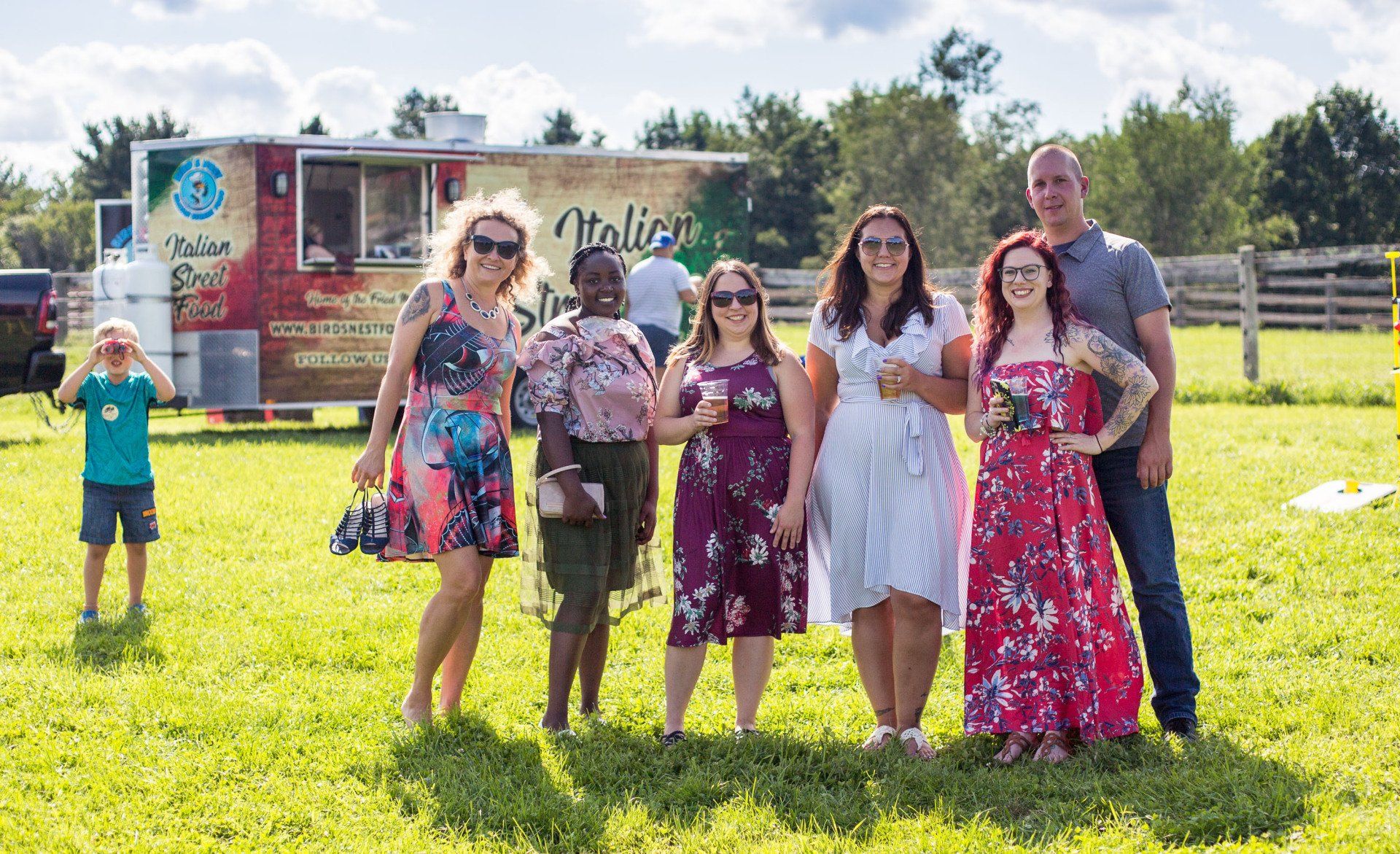 A group of people are standing in a grassy field in front of a food truck.