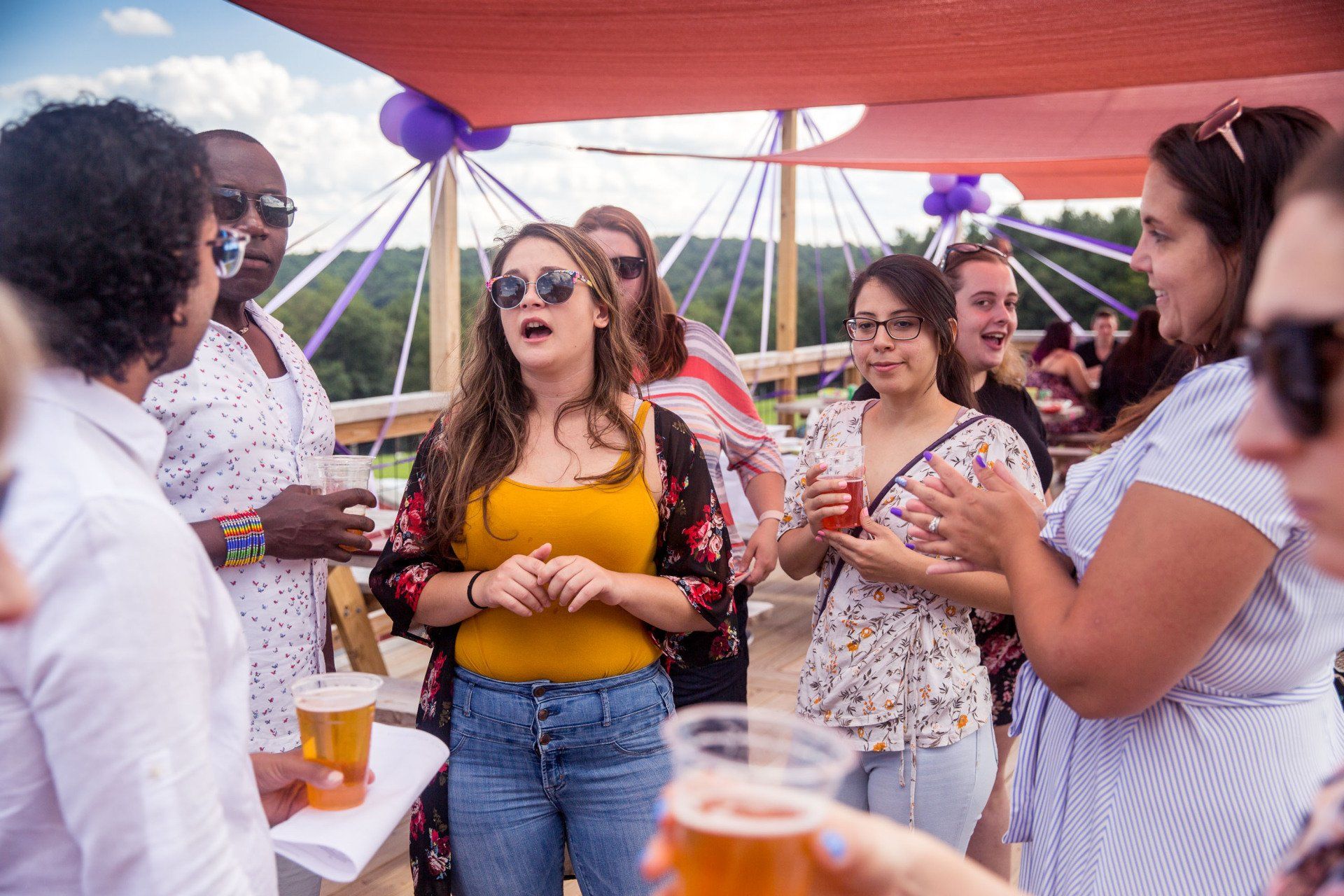 A group of women are standing around a table drinking beer.