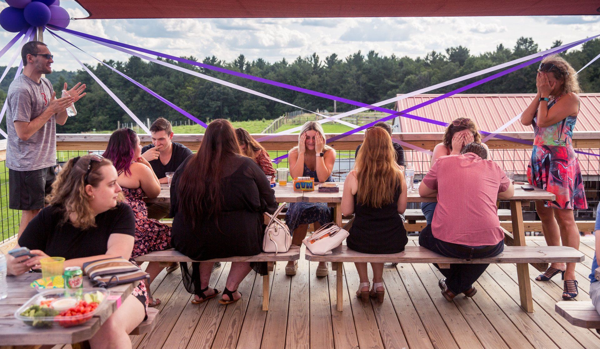 A group of people are sitting at picnic tables on a deck.