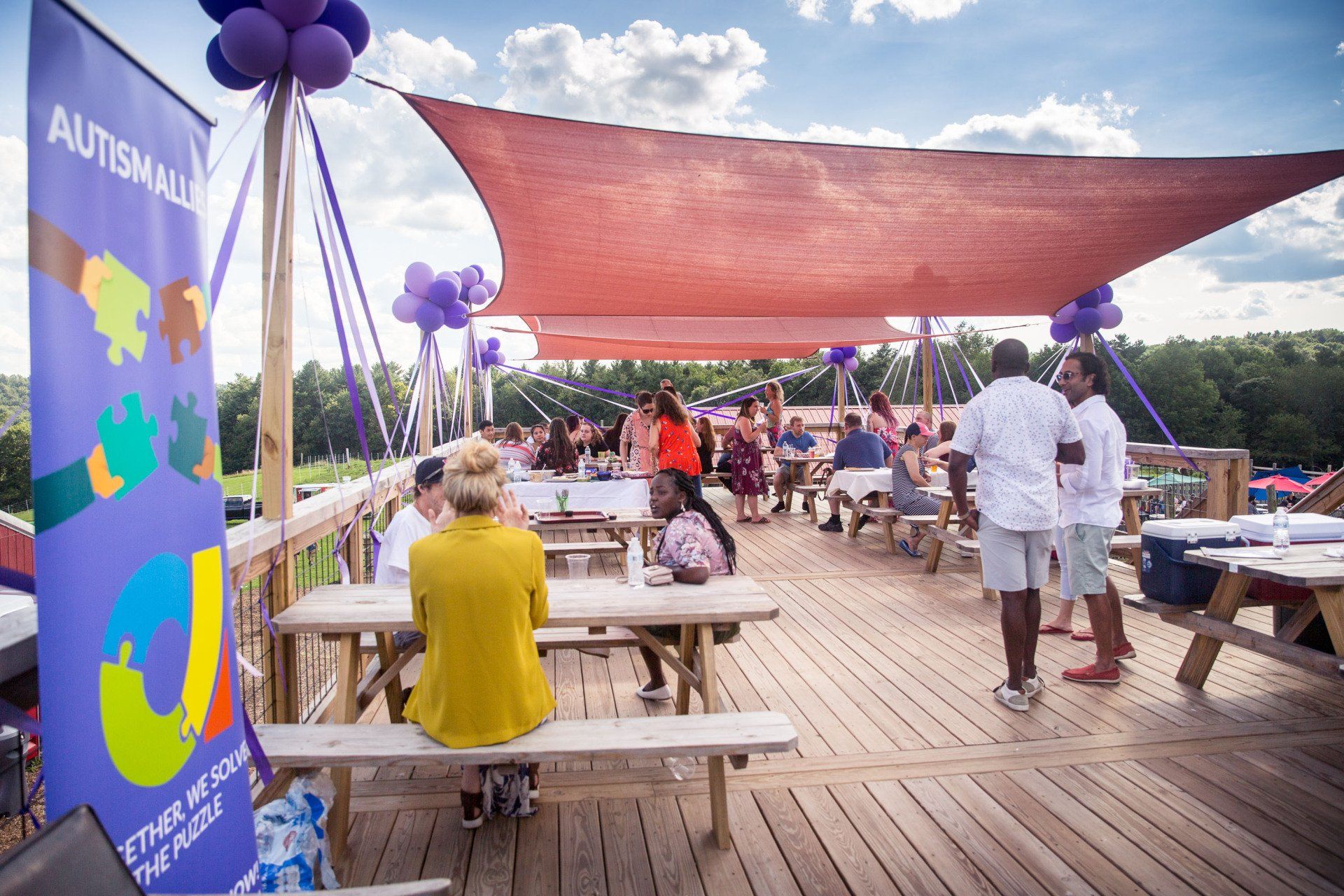A group of people are sitting at picnic tables under a canopy.