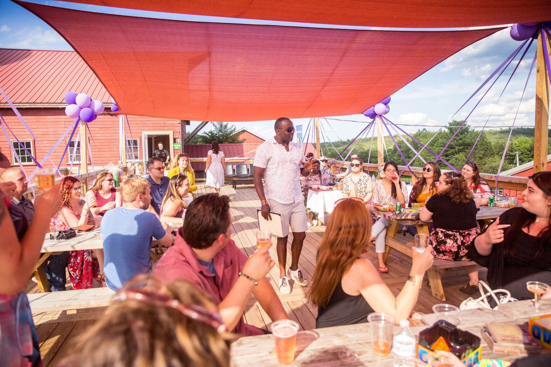 A group of people are sitting at picnic tables under a red umbrella.