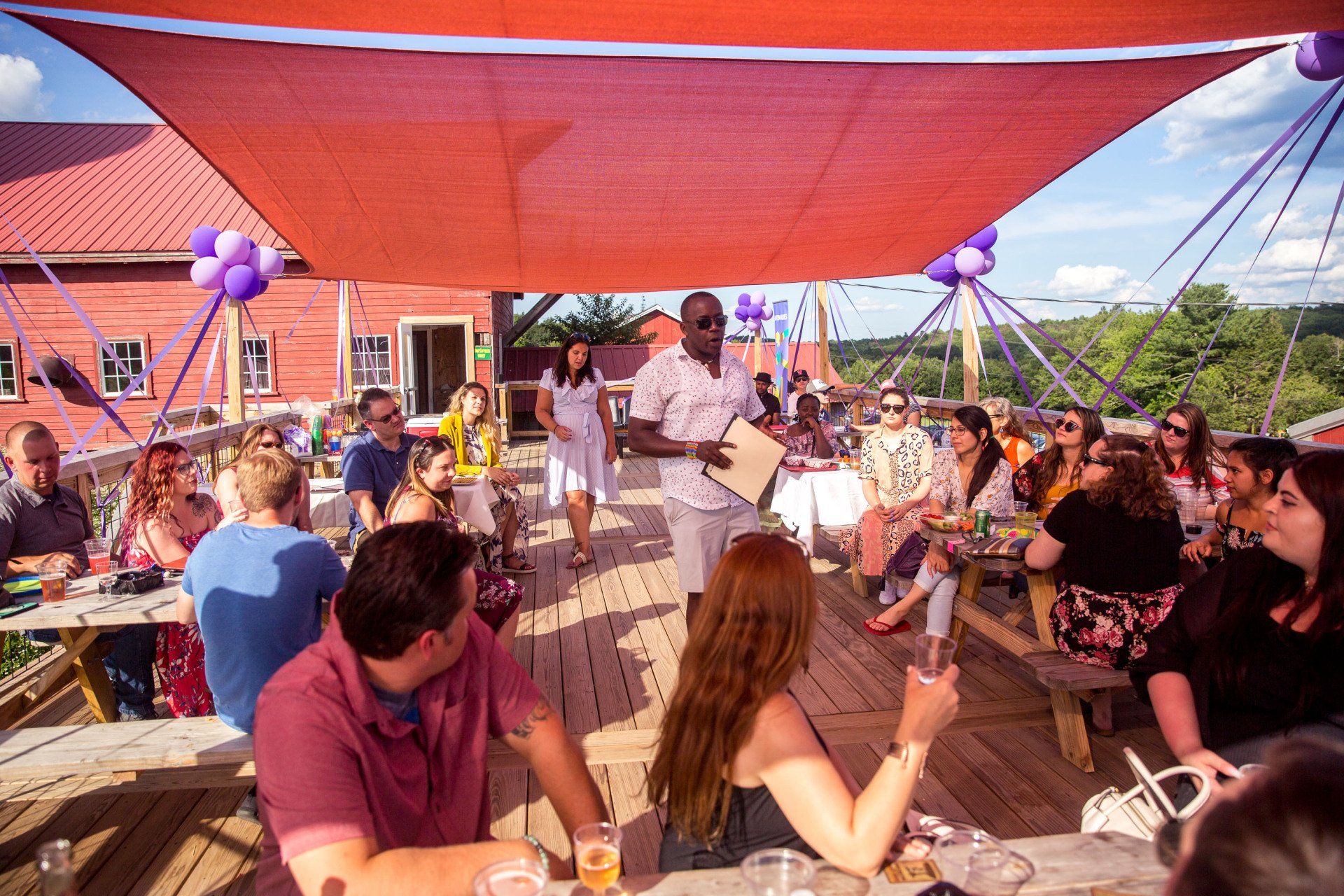 A group of people are sitting at tables under a red umbrella.