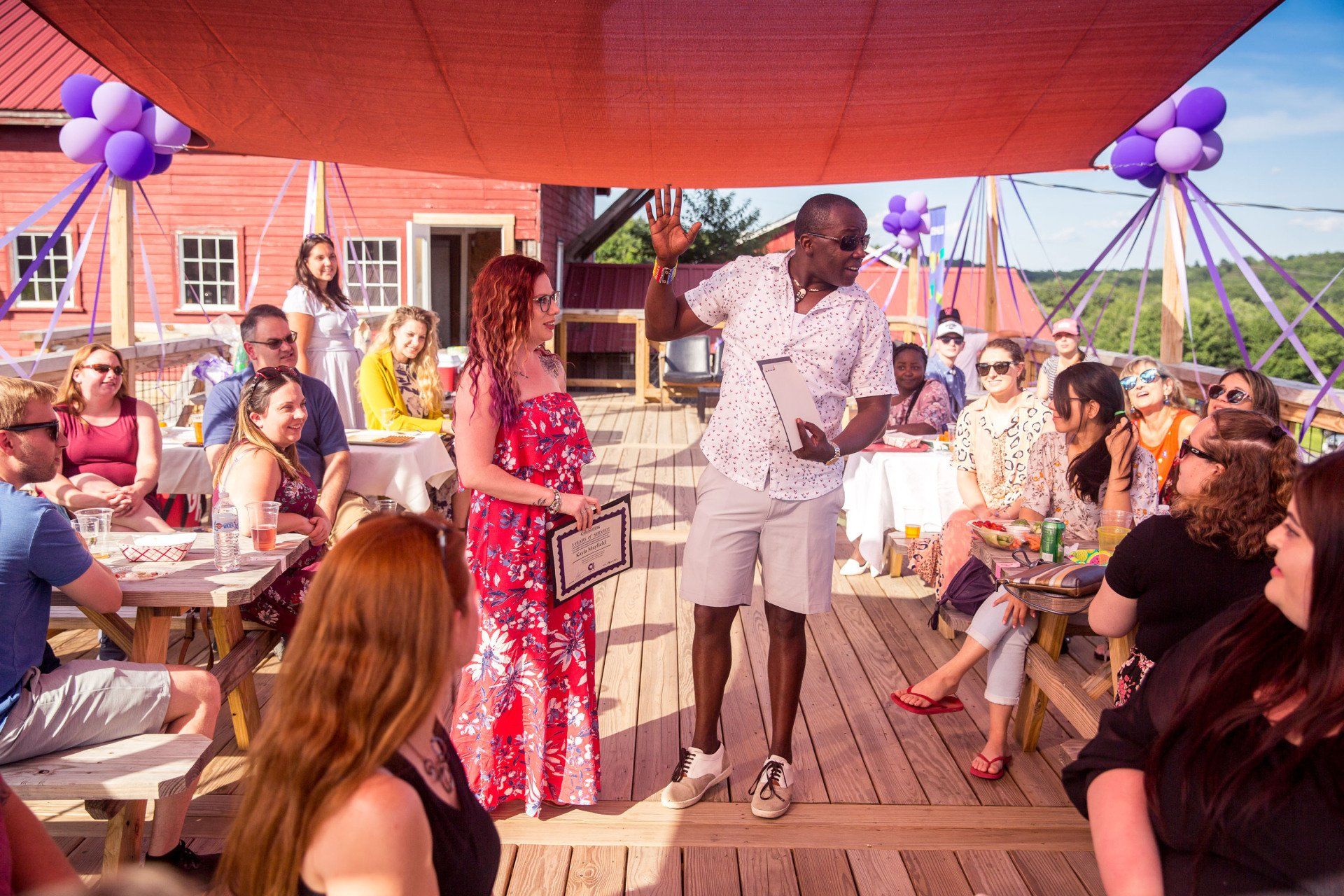 A man and a woman are standing on a deck talking to a group of people.