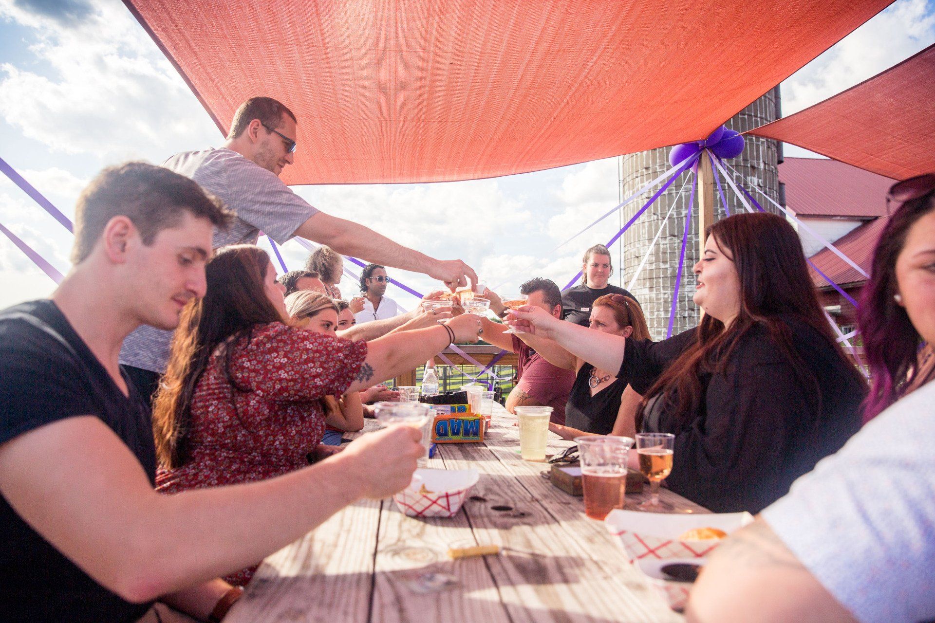 A group of people are sitting at a picnic table toasting with beer.
