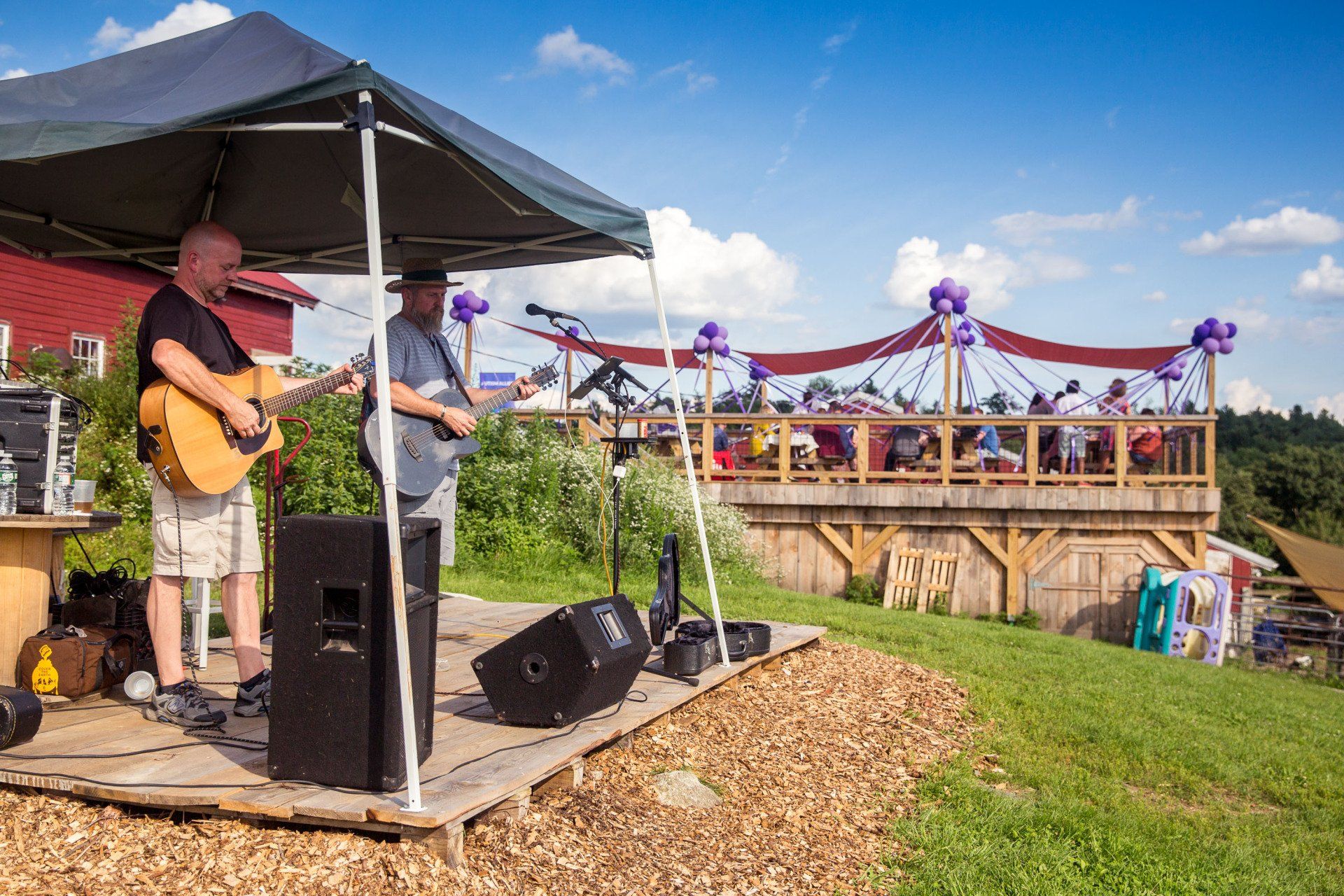 Two men are playing guitars on a stage under a tent.