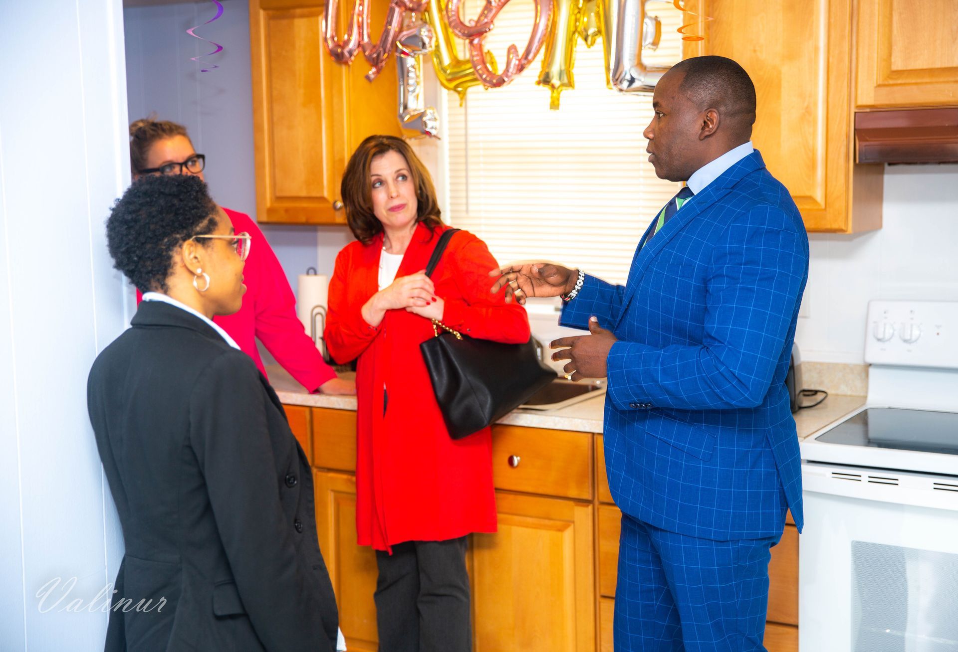 A man in a blue suit is talking to two women in a kitchen.