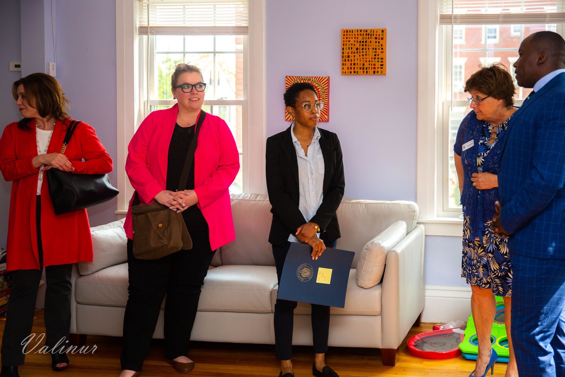 A group of people are standing around a couch in a living room.