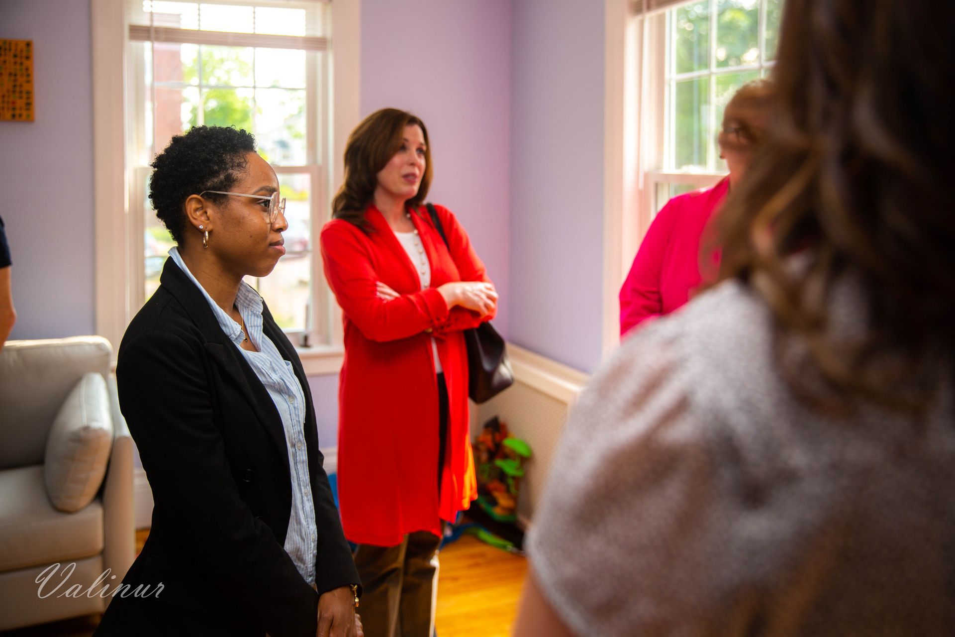 A group of women are standing in a living room talking to each other.