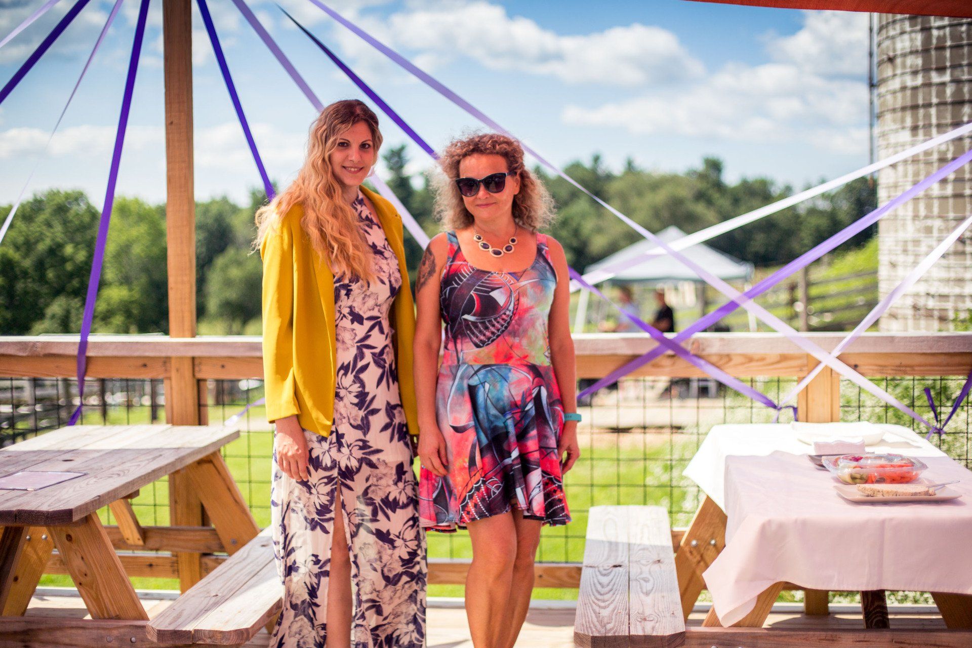Two women are standing next to each other in front of a picnic table.